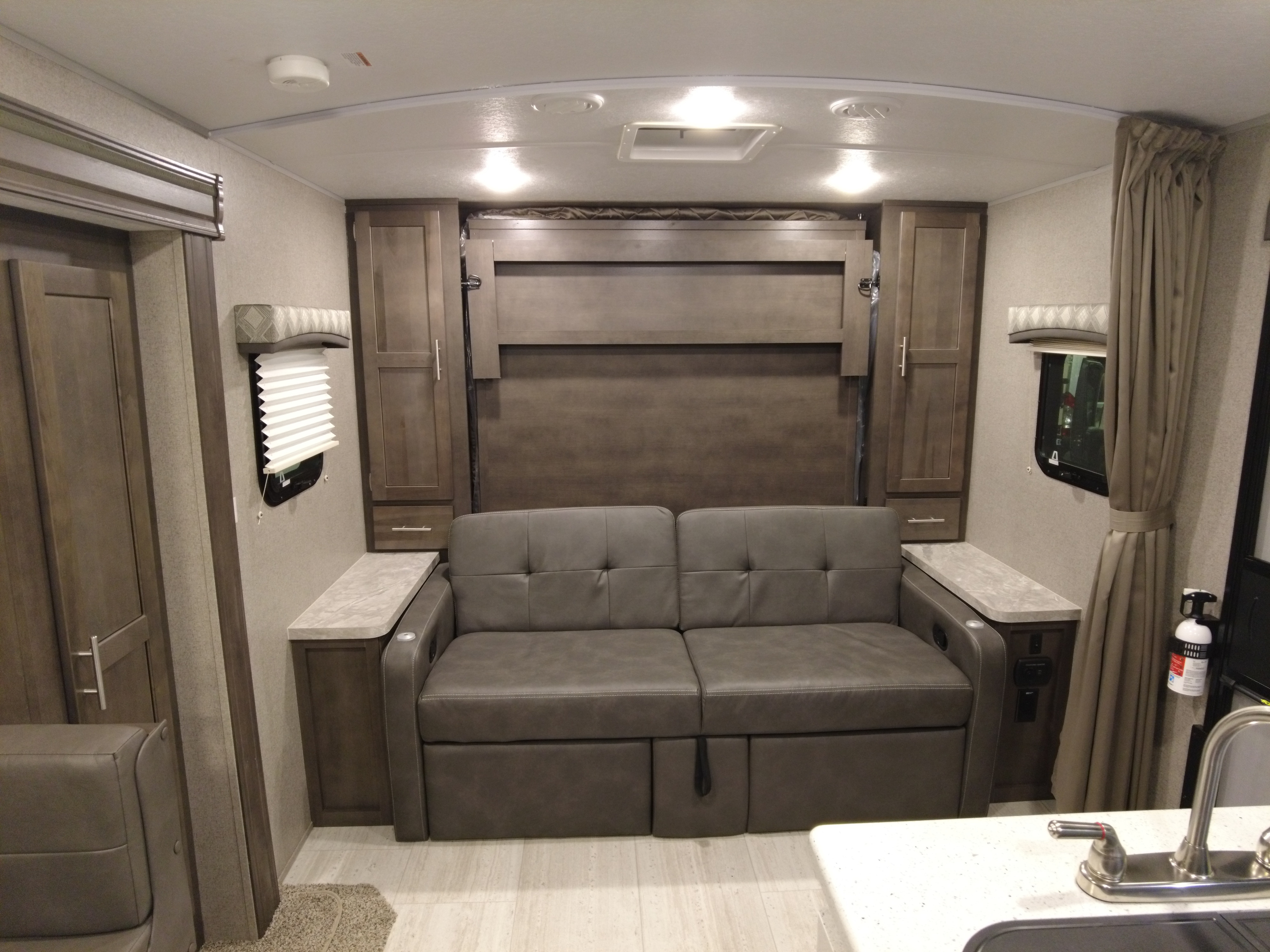 RV rental living area with a gray sofa, murphy bed, cabinets, and partial kitchen view.. Forest River Flagstaff Micro Lite 2021