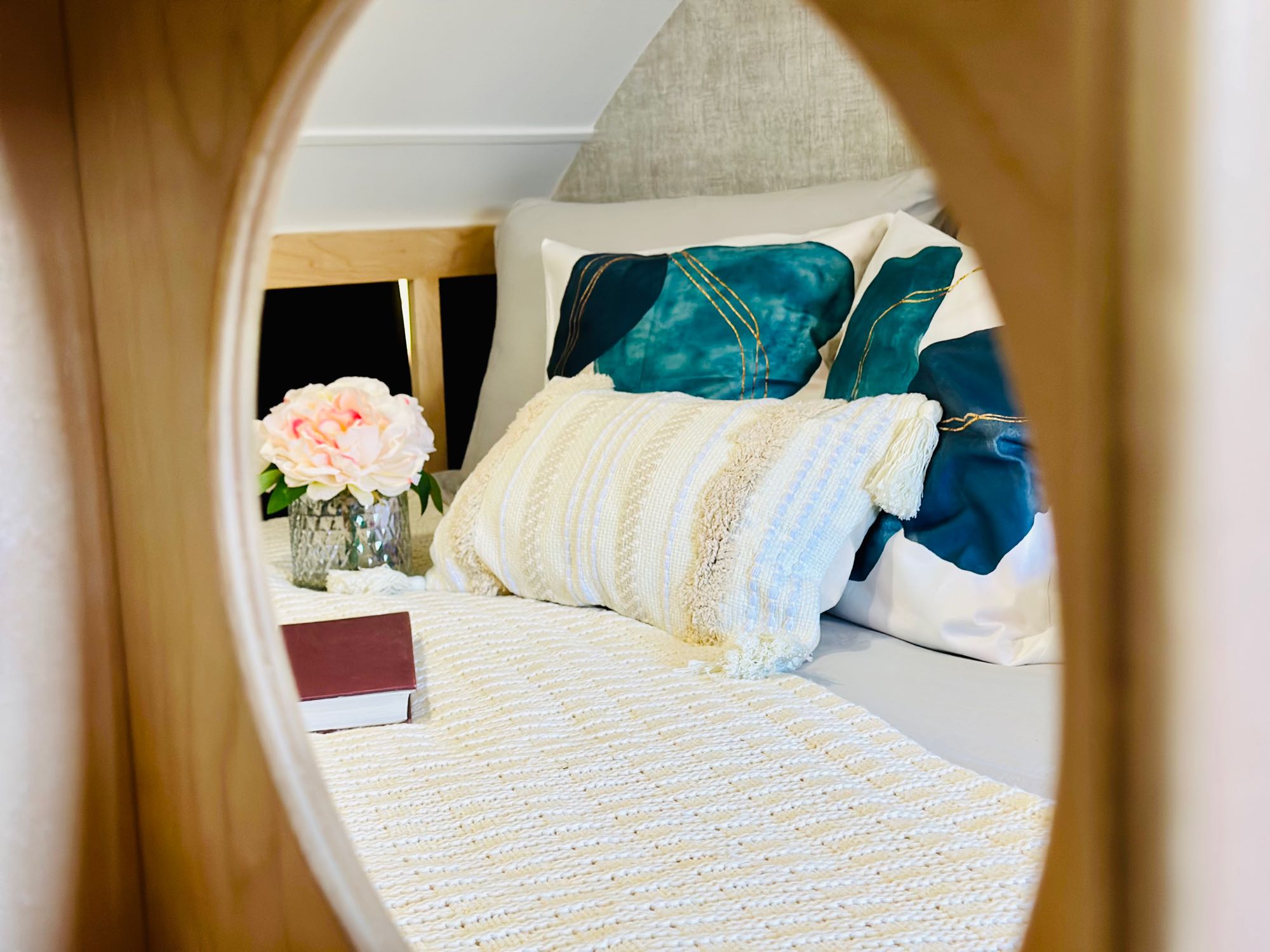 Inside a luxurious rv rental: a cozy bedroom with chic teal and white pillows, a soft blanket, and a floral vase.. Little Guy Micro Max 2023