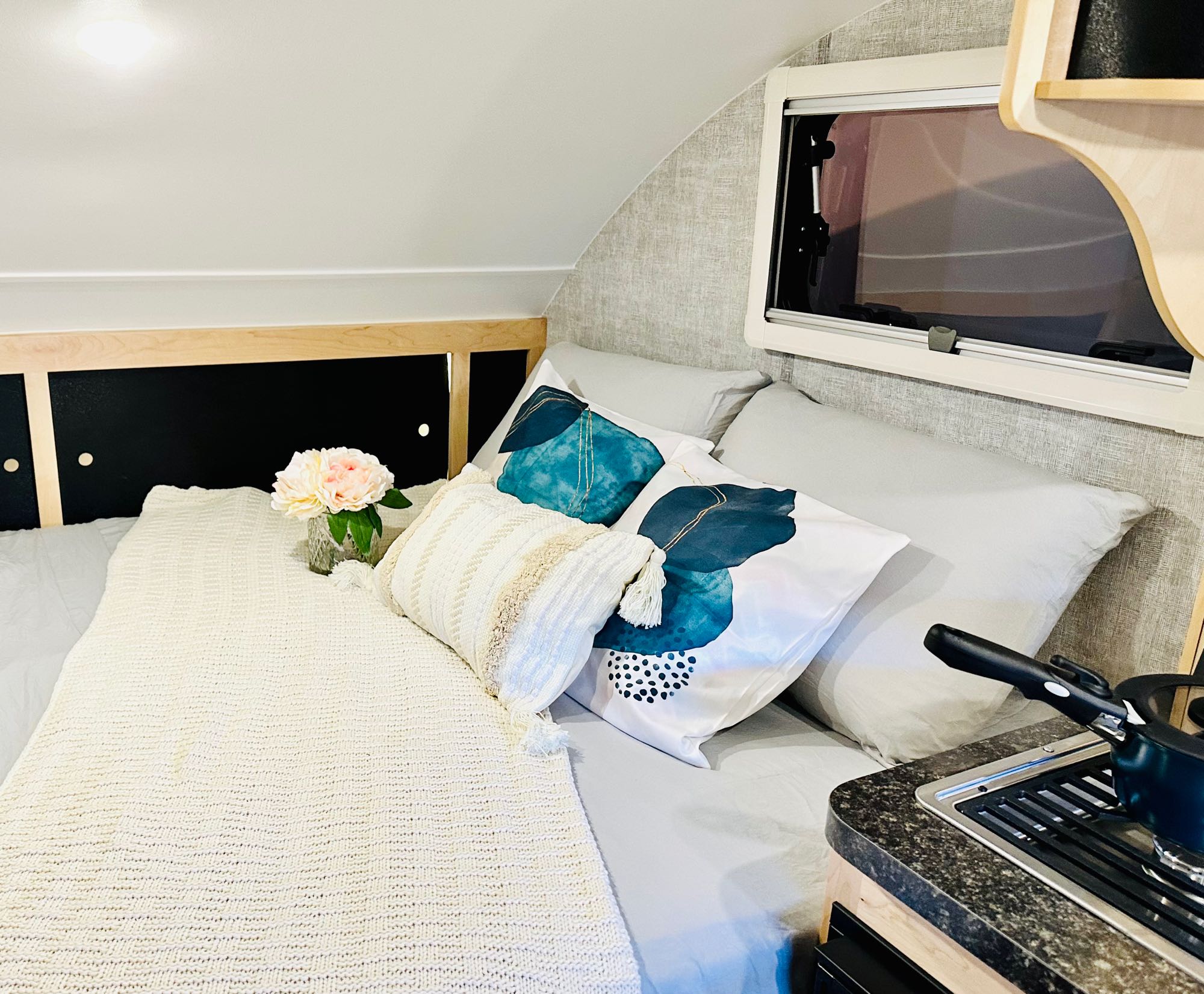 Relax in this RV rental's cozy bed with vibrant pillows, next to a compact kitchen.. Little Guy Micro Max 2023