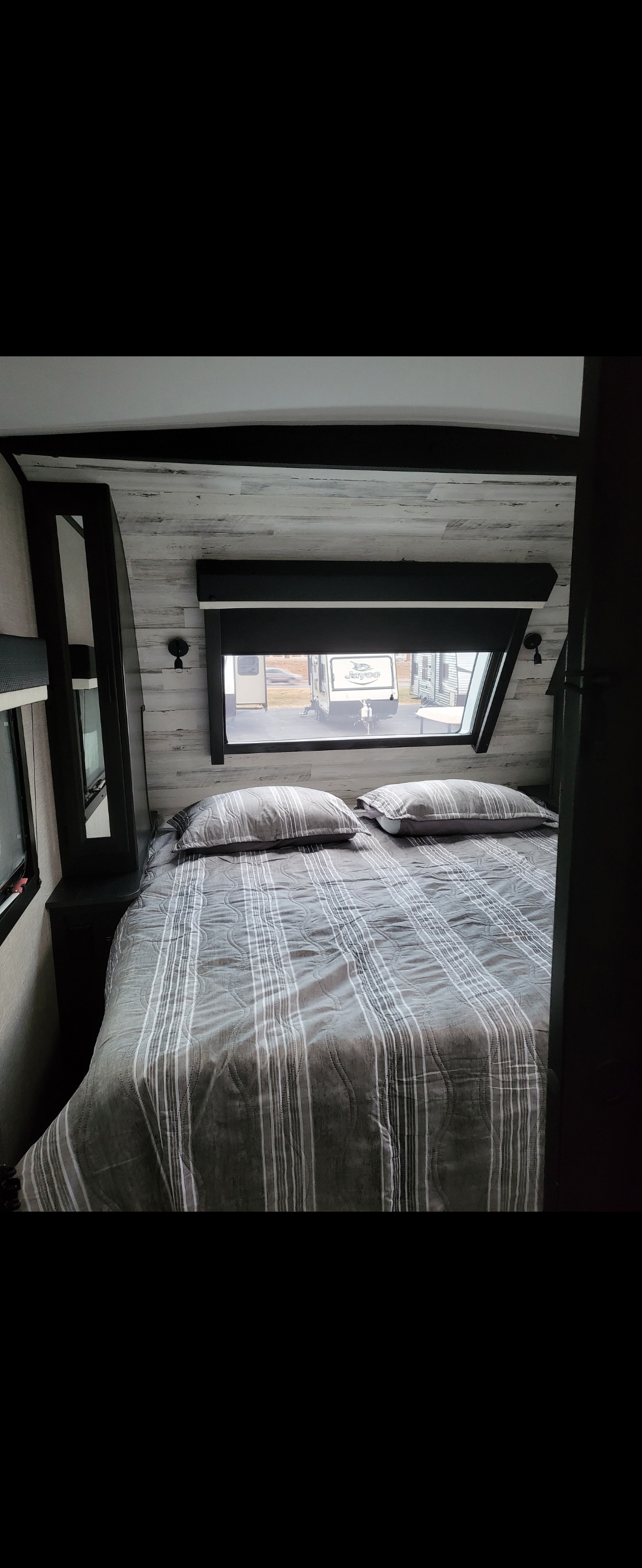 Cozy RV rental bedroom with striped queen bed, window view, and wood-look walls. Perfect for travel trailer trips.. Jayco White Hawk 2022