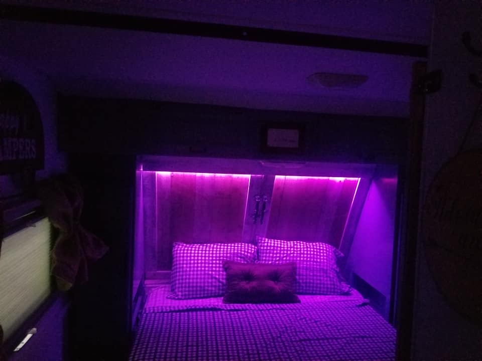A cozy RV rental bedroom. It features a bed with checkered bedding, framed by purple LED strip lighting and wood panels.. Fleetwood WILDERNESS 2000