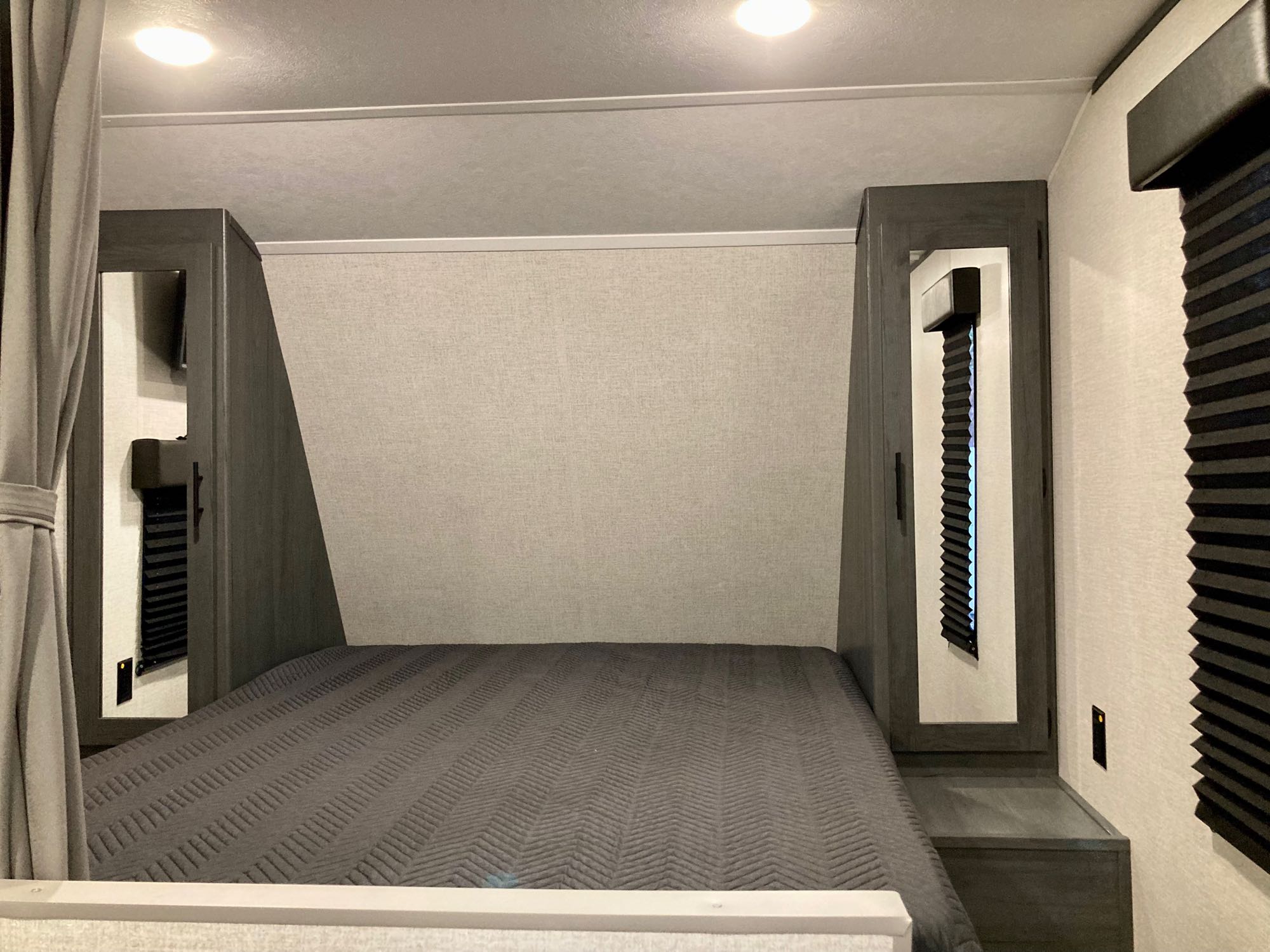 Comfortable RV rental bedroom featuring a gray bed, built-in side cabinets, overhead lights, and blackout blinds.. Colorado Colorado Trailer 2022