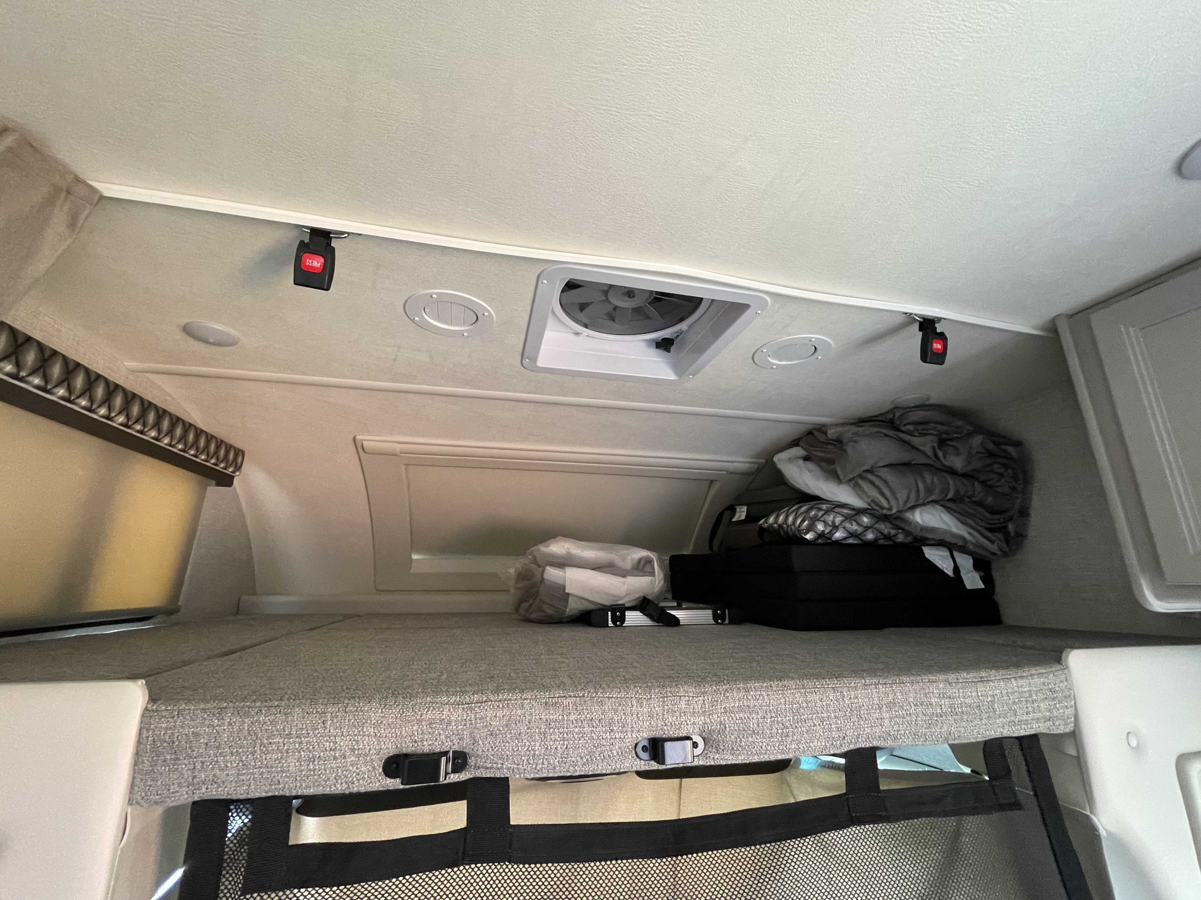 Overhead bunk in an RV rental, with blankets, bags, and safety buckles visible, alongside ceiling fan and vents.. Thor Quantum 2022