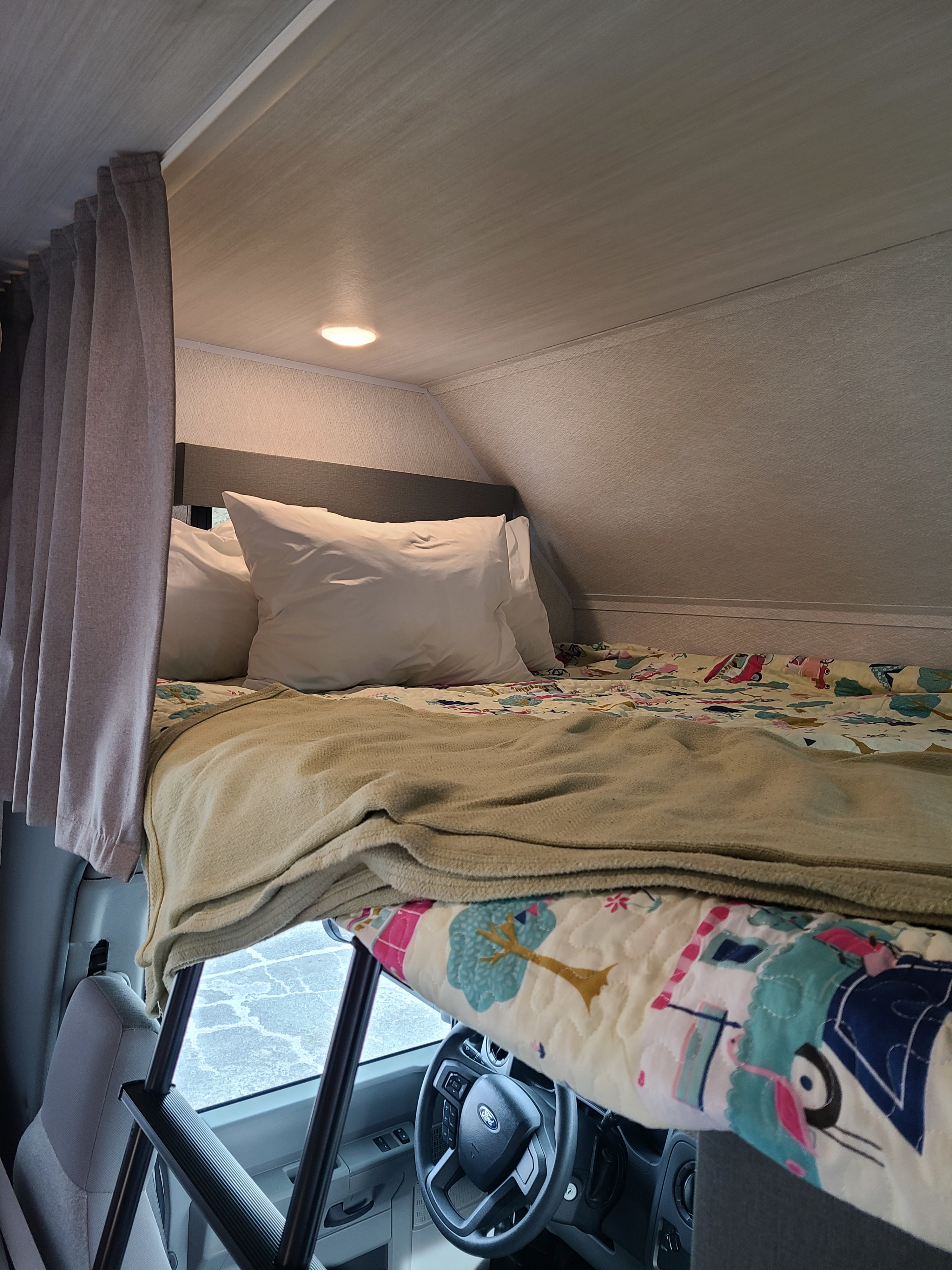 Cozy RV rental cab-over bunk with a colorful bed, access ladder, and driver's area visible below.. East to West Entrada 2023