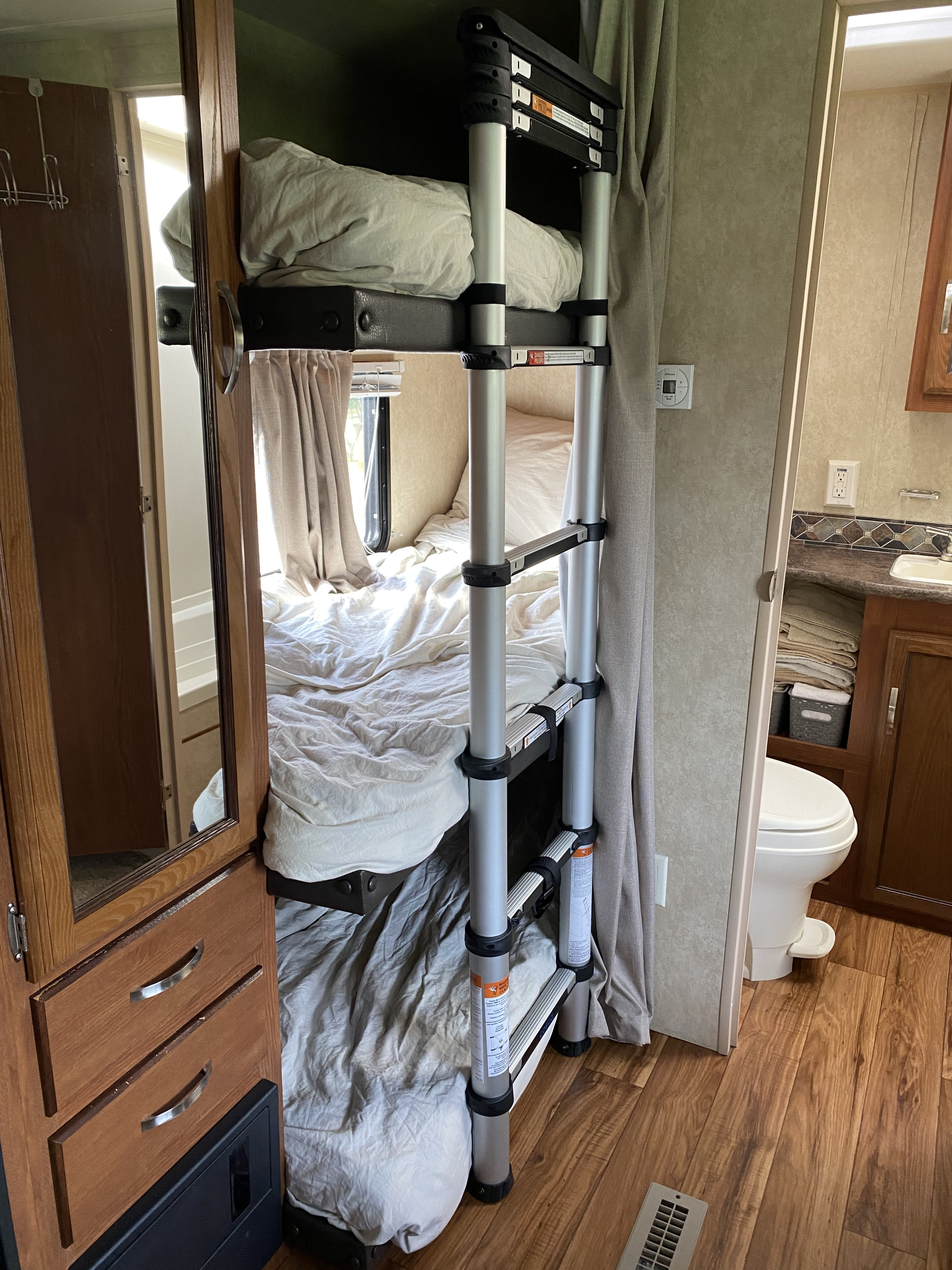 Cozy RV rental interior featuring comfortable bunk beds with a ladder, and a compact bathroom area. Ideal for family adventures.. Forest River Salem 2015