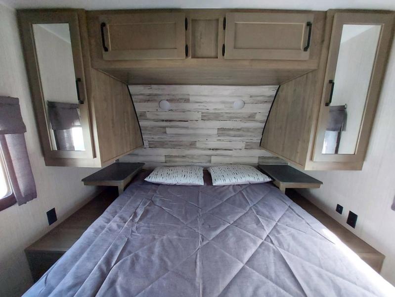 This RV rental bedroom features a comfortable bed with purple bedding, overhead cabinets, and mirrored side wardrobes.. Forest River Palomino Puma 2022