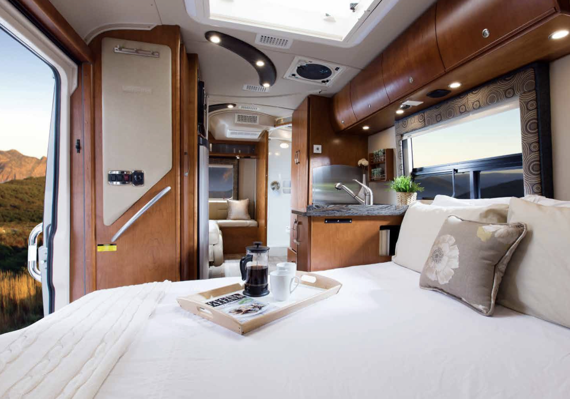 Luxurious RV rental interior featuring a spacious bed, kitchen area, and mountain views outside.. Leisure Travel Van Serenity 2014