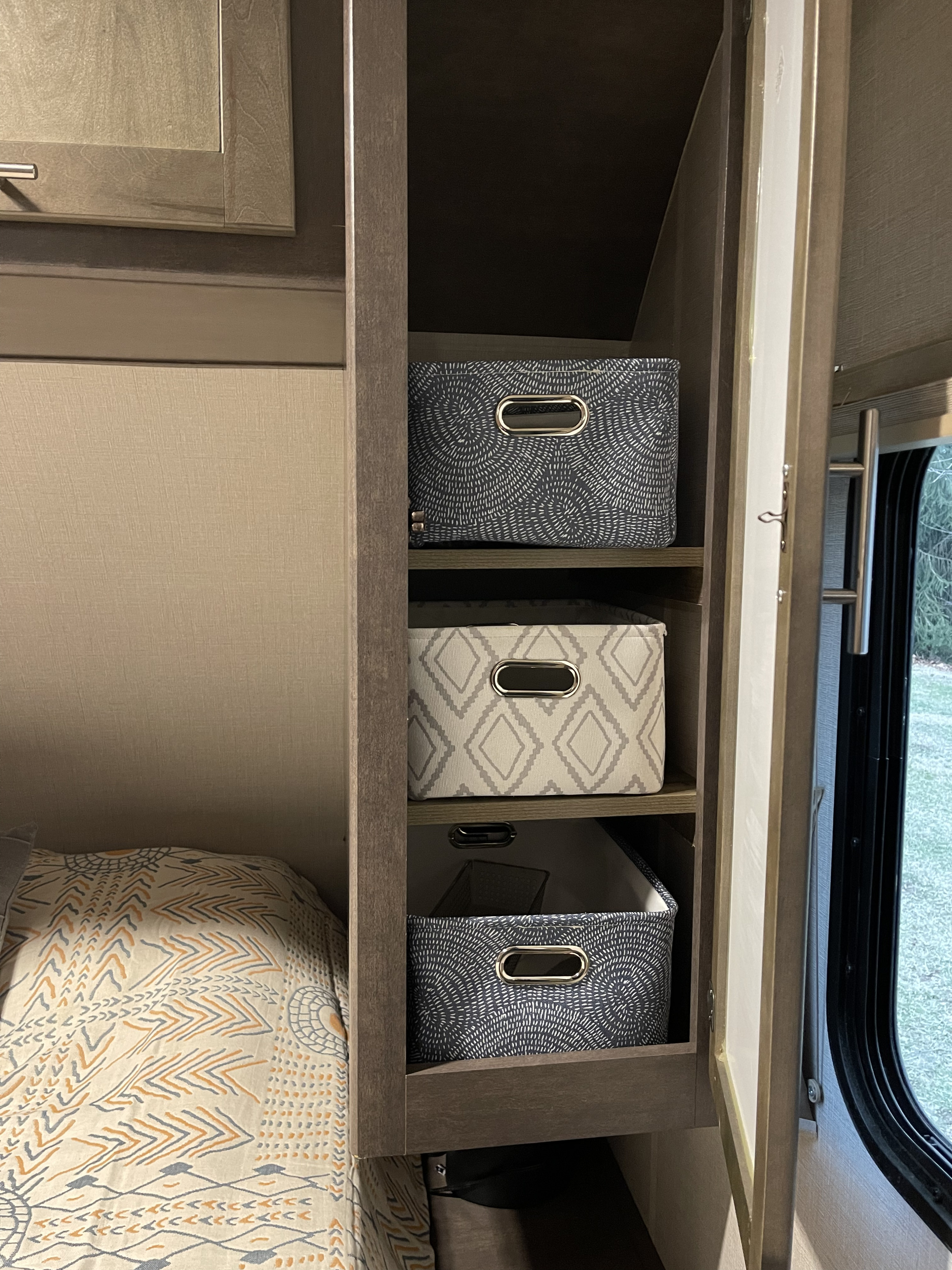 Stay organized in your RV rental with built-in storage shelves and patterned fabric bins, next to a cozy bed.. Crossroads RV Sunset Trail Super Lite 2018