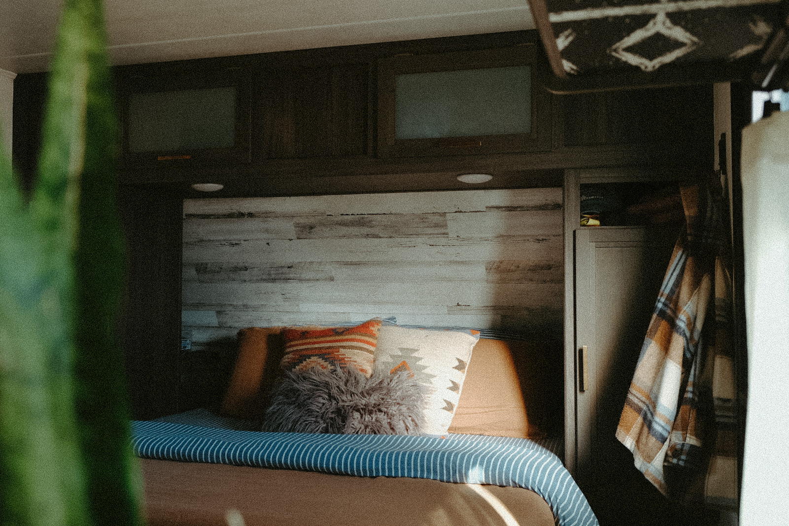 Inside a cozy RV rental bedroom: bed with decorative pillows, wood headboard, and built-in storage with a plaid blanket.. Dutchmen Kodiak Cub 2020