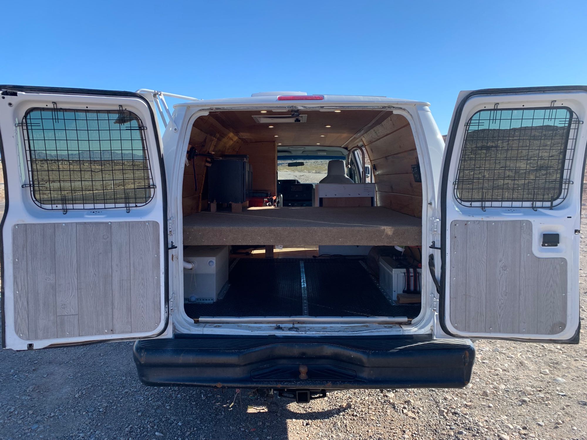 An RV rental camper van conversion reveals its rear interior with a raised bed platform and organized storage below.. Ford Ford E350 2011