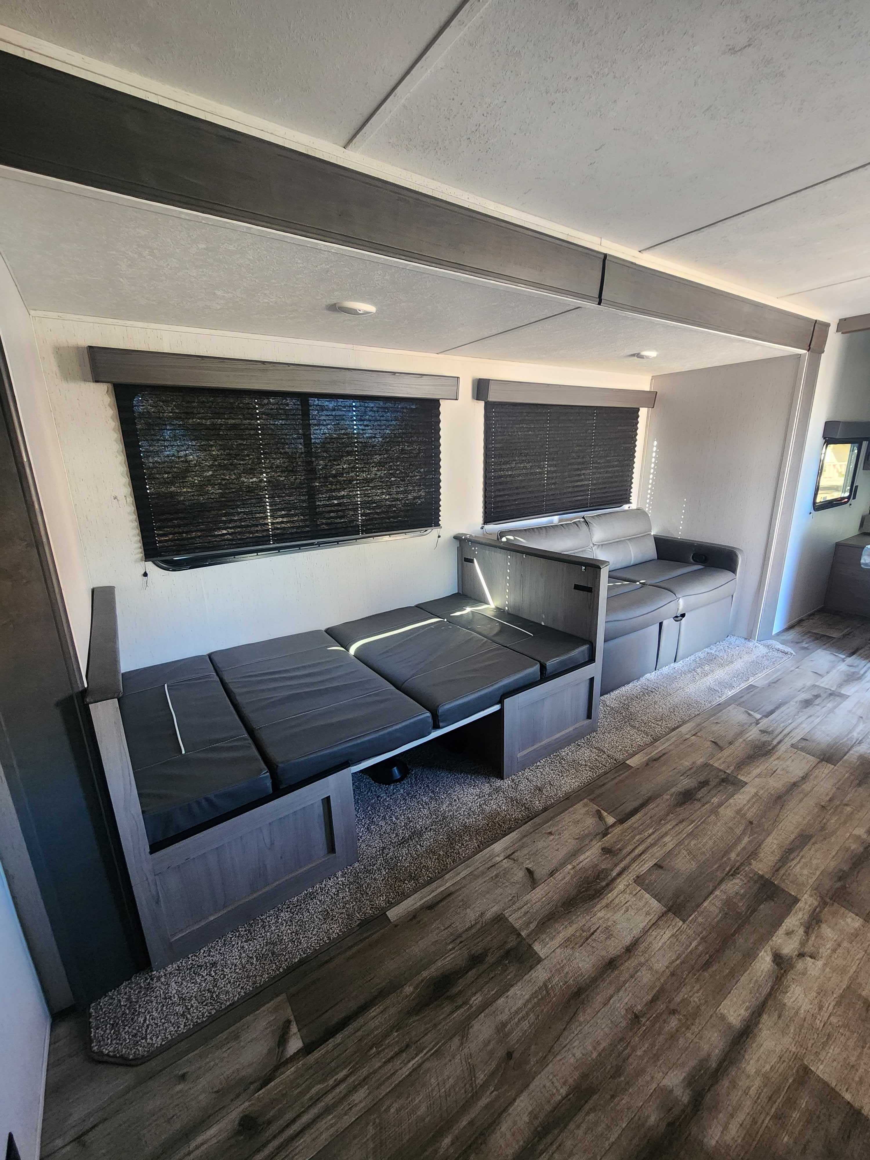 RV rental interior: Dinette converts to a bed with dark cushions, warm wood flooring, and privacy blinds. Spacious & ready for travel.. Dutchmen Coleman Lantern LT 2022