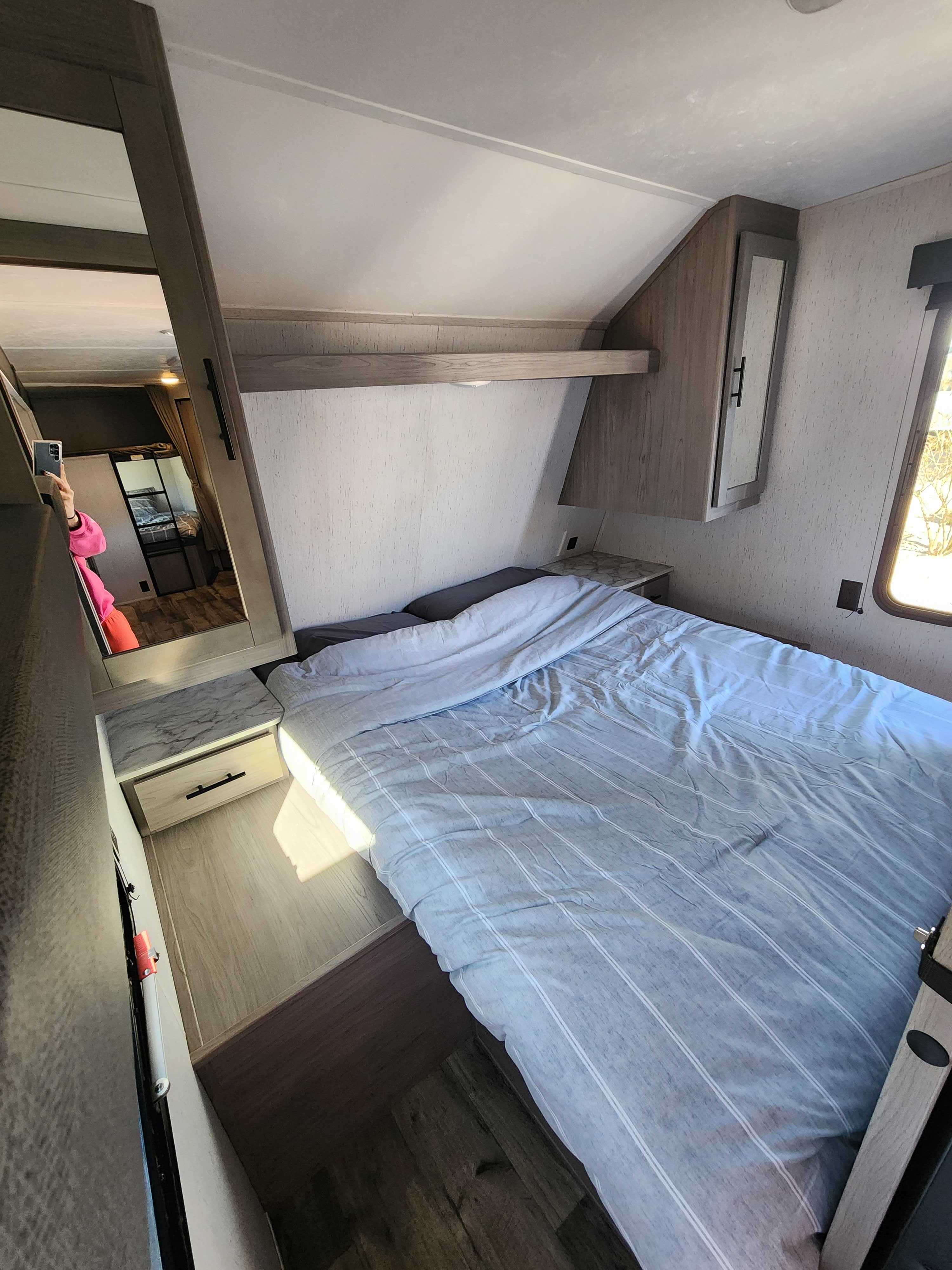 Comfortable RV rental bedroom with a striped bed, modern nightstand, and mirrored cabinet, reflecting the interior.. Dutchmen Coleman Lantern LT 2022