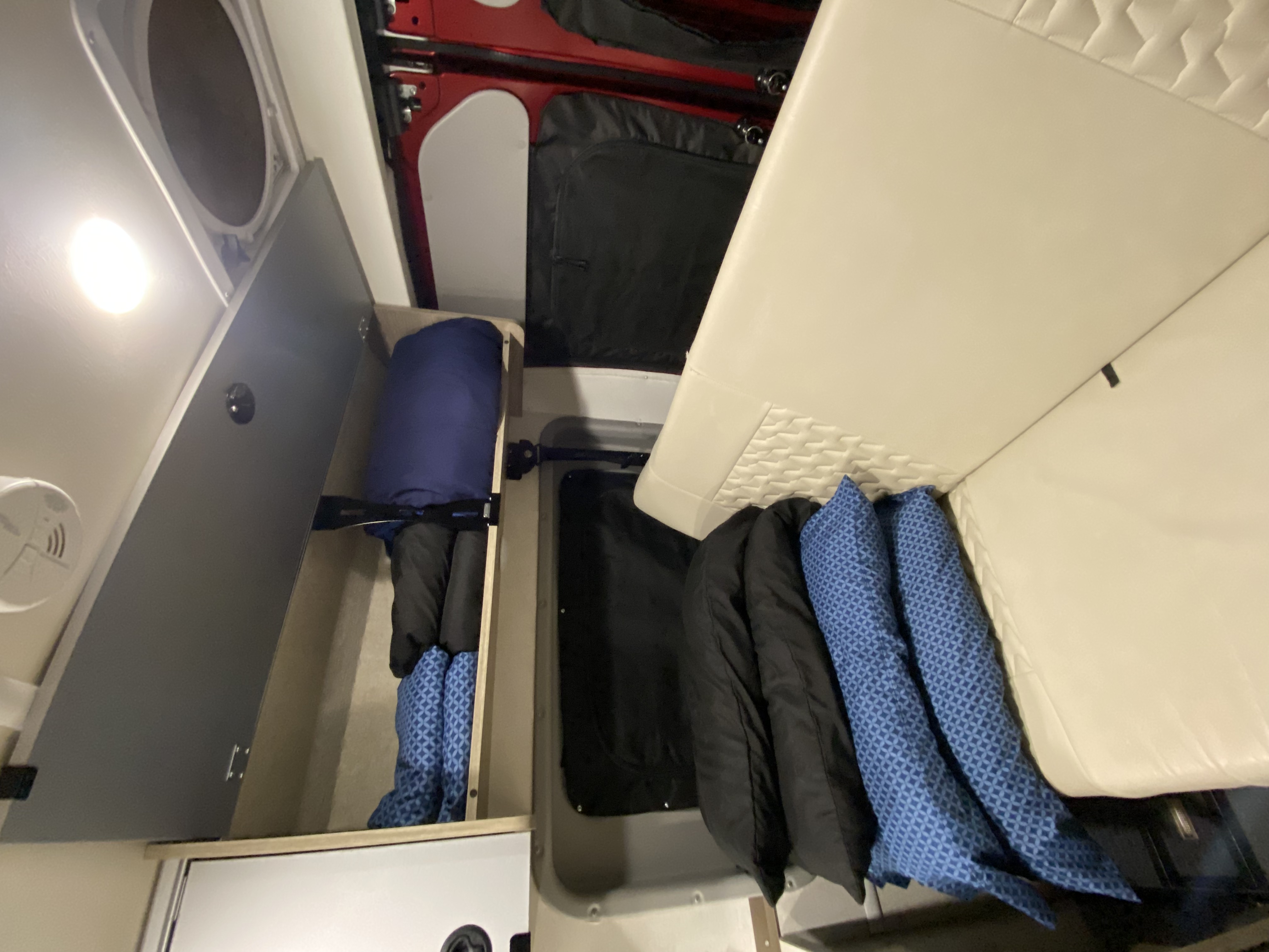 Interior of an rv rental showing plush seating, organized storage below, an overhead cabinet, and a smoke detector.. Winnebago Solis 59P 2021