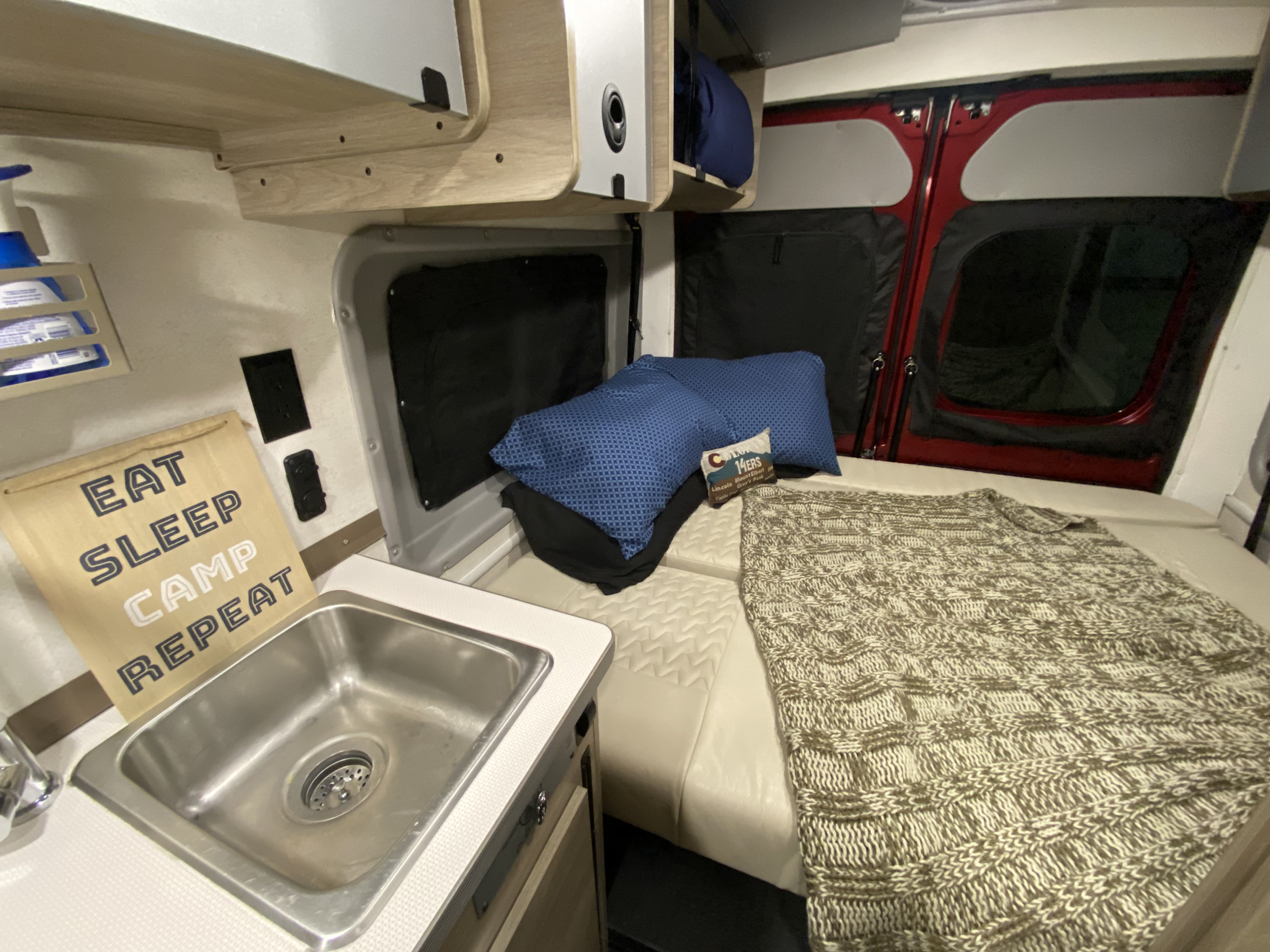 Inviting rv rental interior: bed, sink, storage, and a "Eat Sleep Camp Repeat" sign. Ready for adventure!. Winnebago Solis 59P 2021