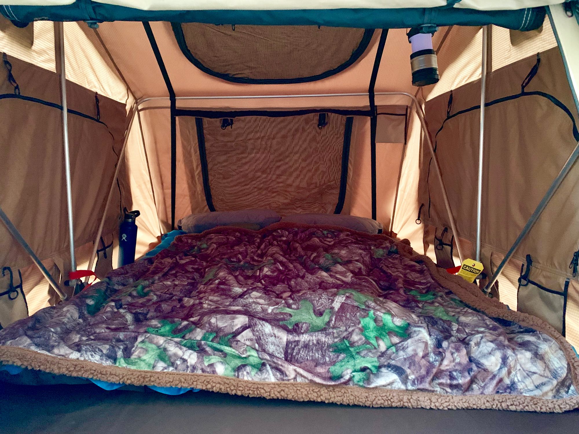 Plush camping bed inside a spacious tent, ideal for RV rental adventures. Features a cozy blanket, pillows, and lantern.. Valiant trailer 2019
