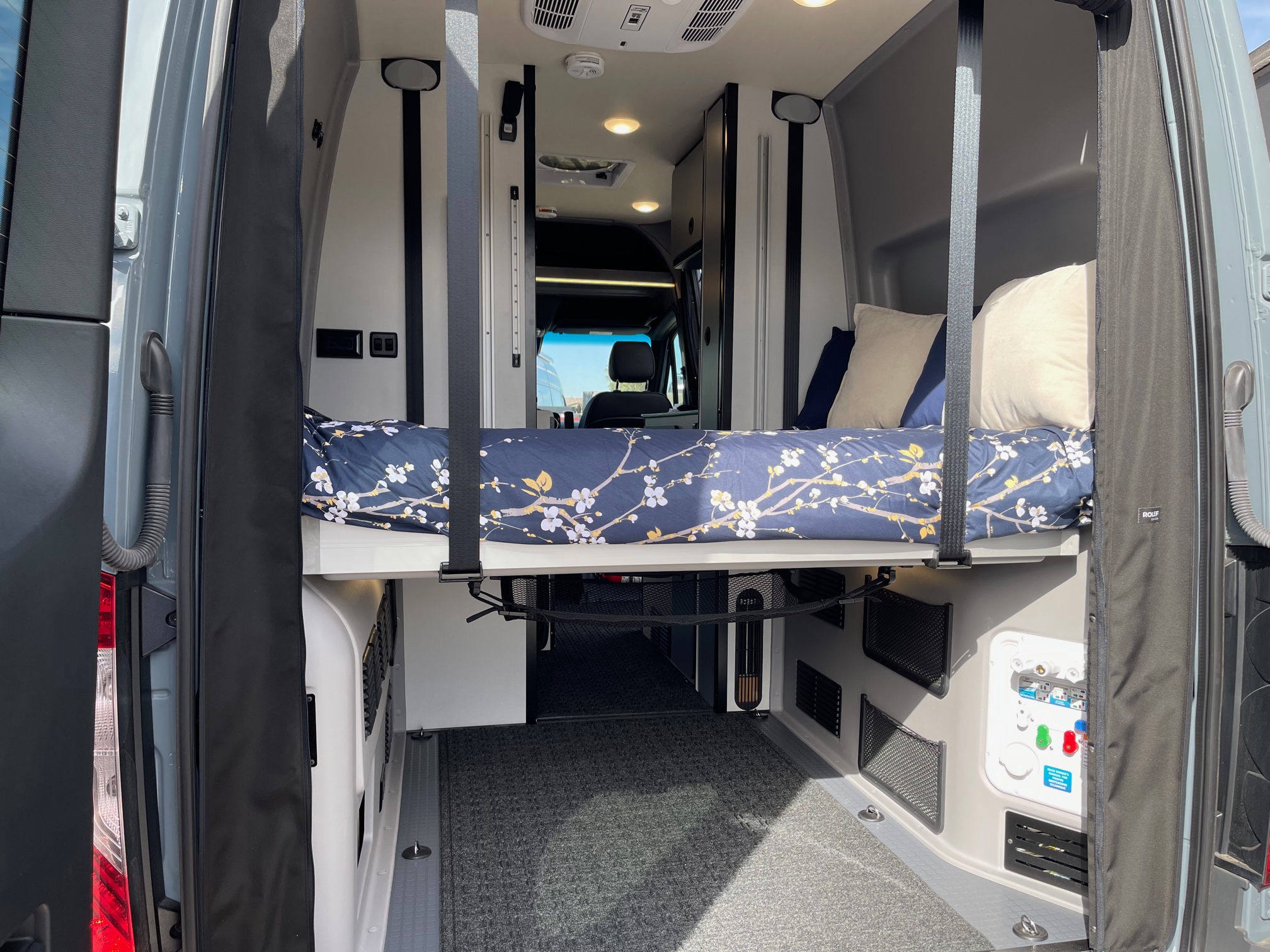 Inside an RV rental: A clever raised bed over a large cargo space, equipped with controls, perfect for van life adventures.. Winnebago Revel 2023