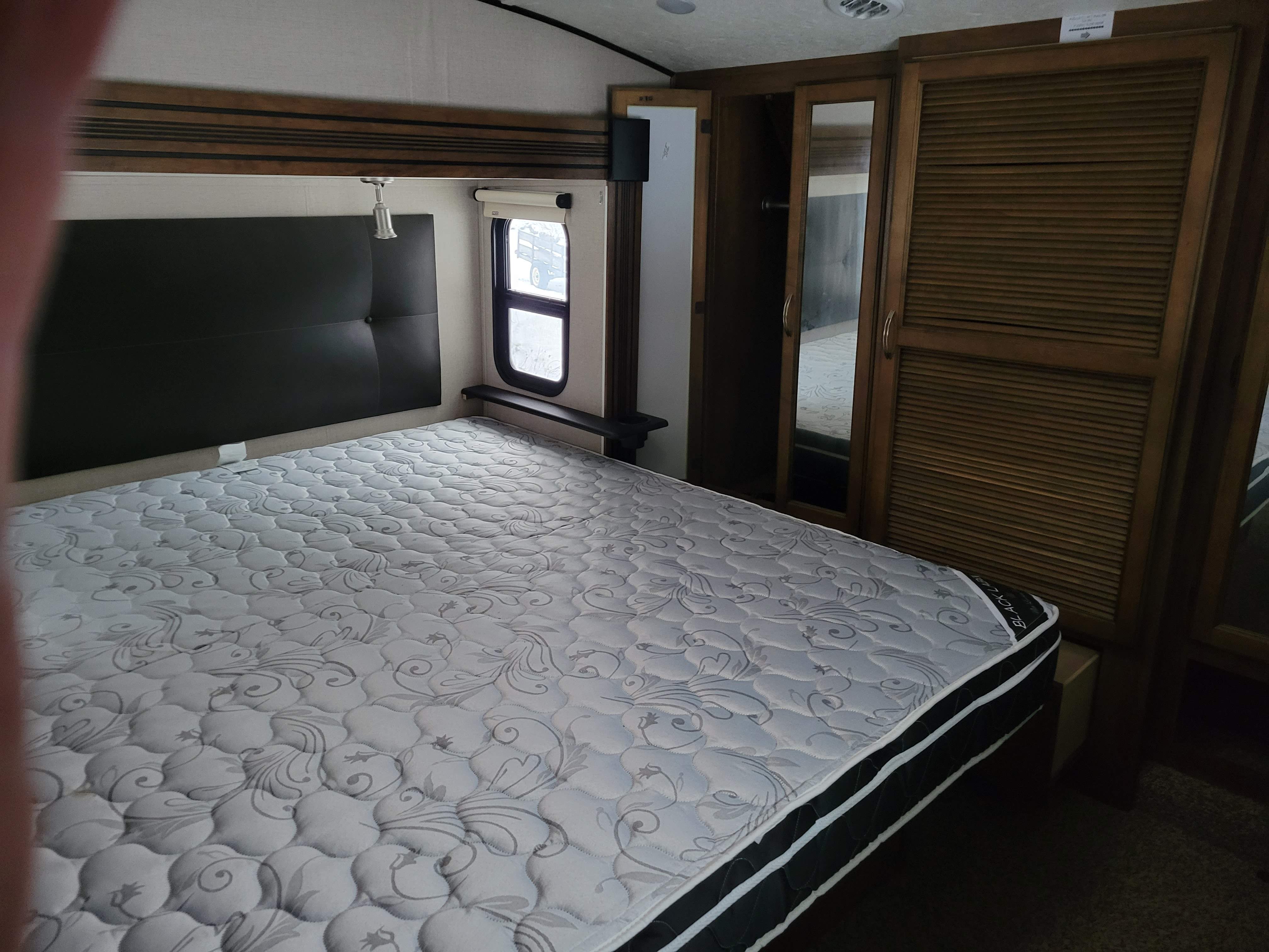 Cozy RV rental bedroom with a comfortable patterned mattress, black headboard, side window, and built-in storage.. Forest River Chaparral 2018