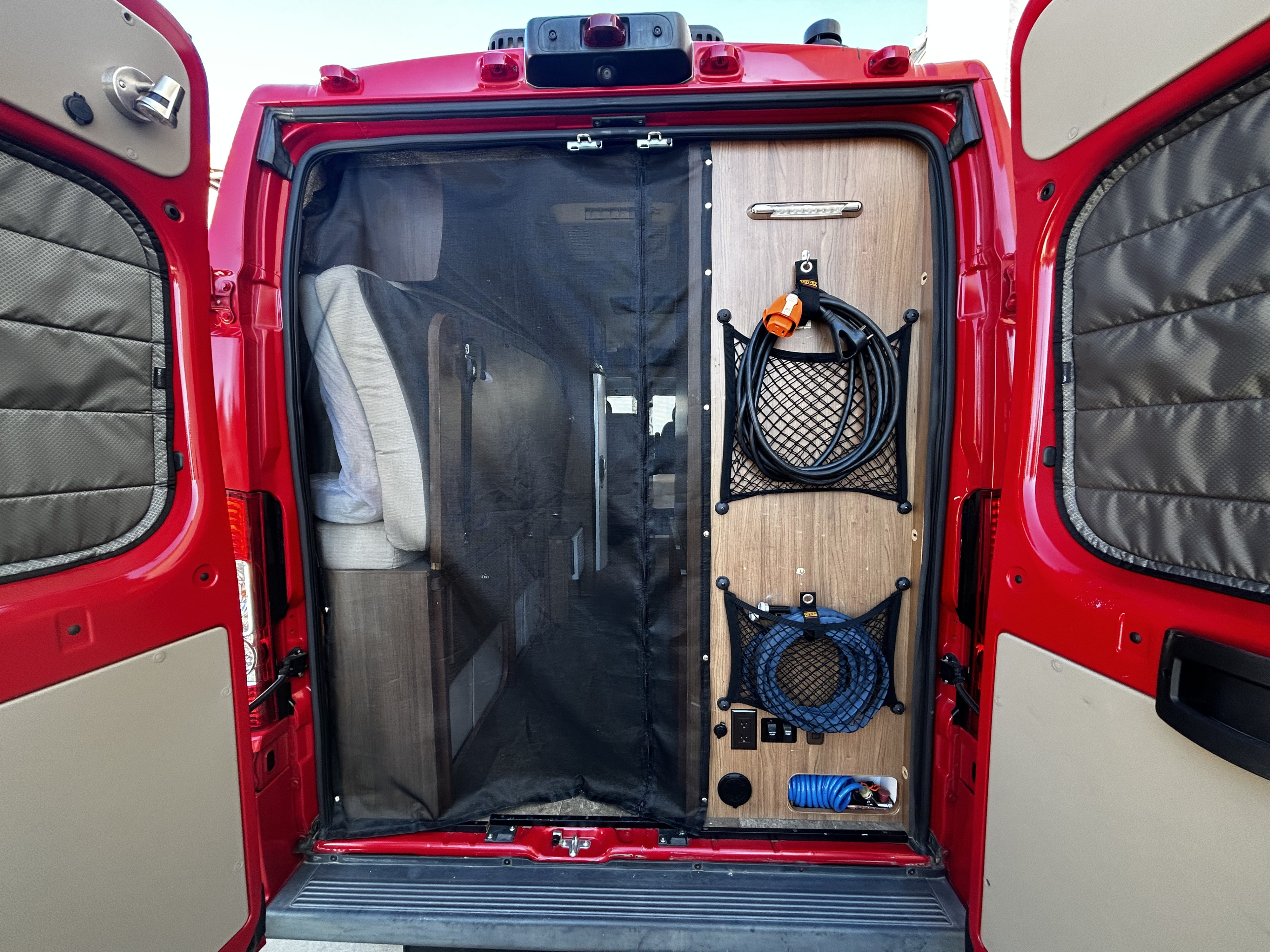 RV rental camper van's open rear showing a bug screen, organized storage for power and water hoses.. Winnebago Travato 2015