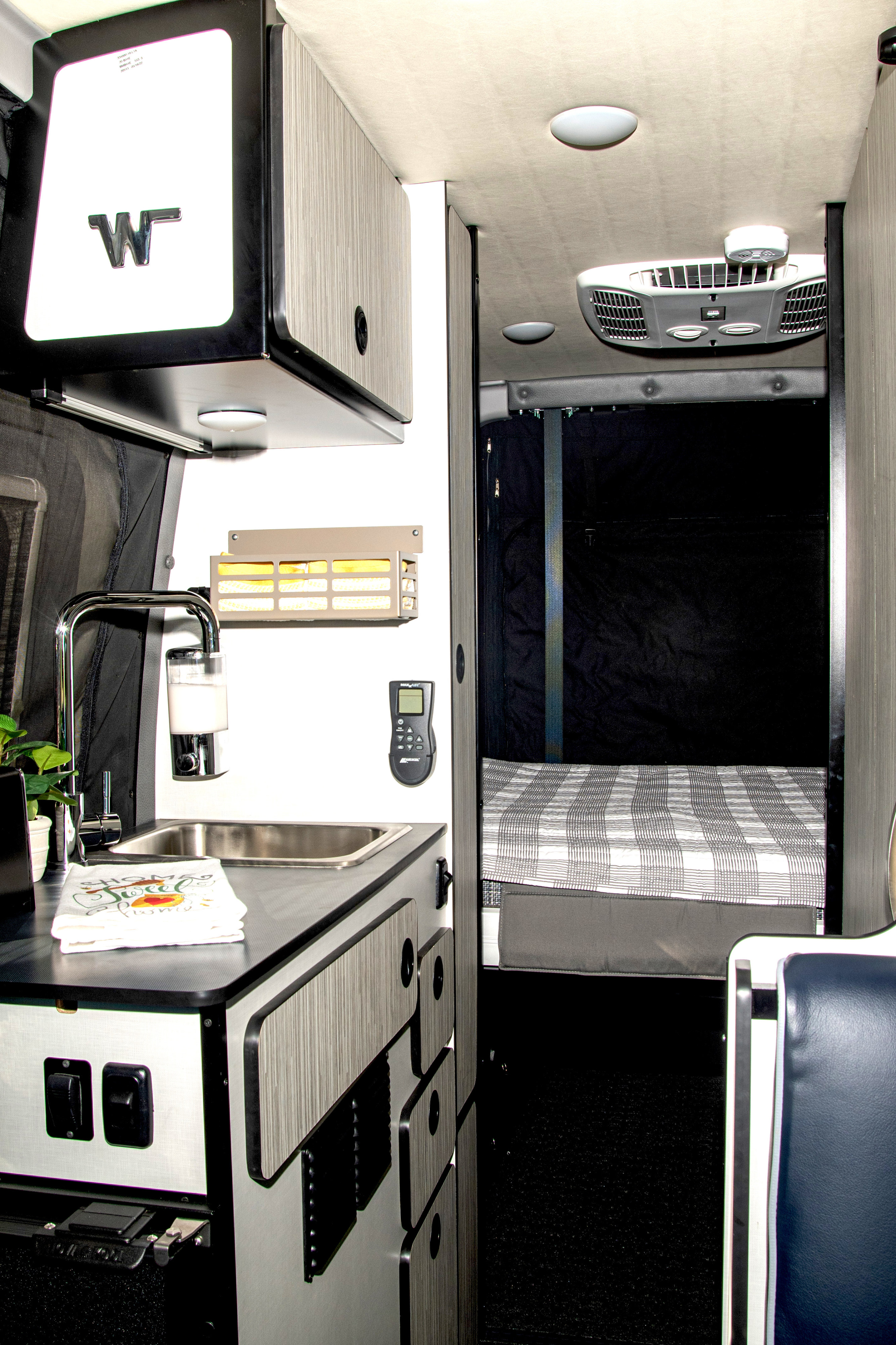 Experience a well-equipped RV rental interior featuring a functional kitchenette, comfy bed, and climate control.. Winnebago Revel 2023