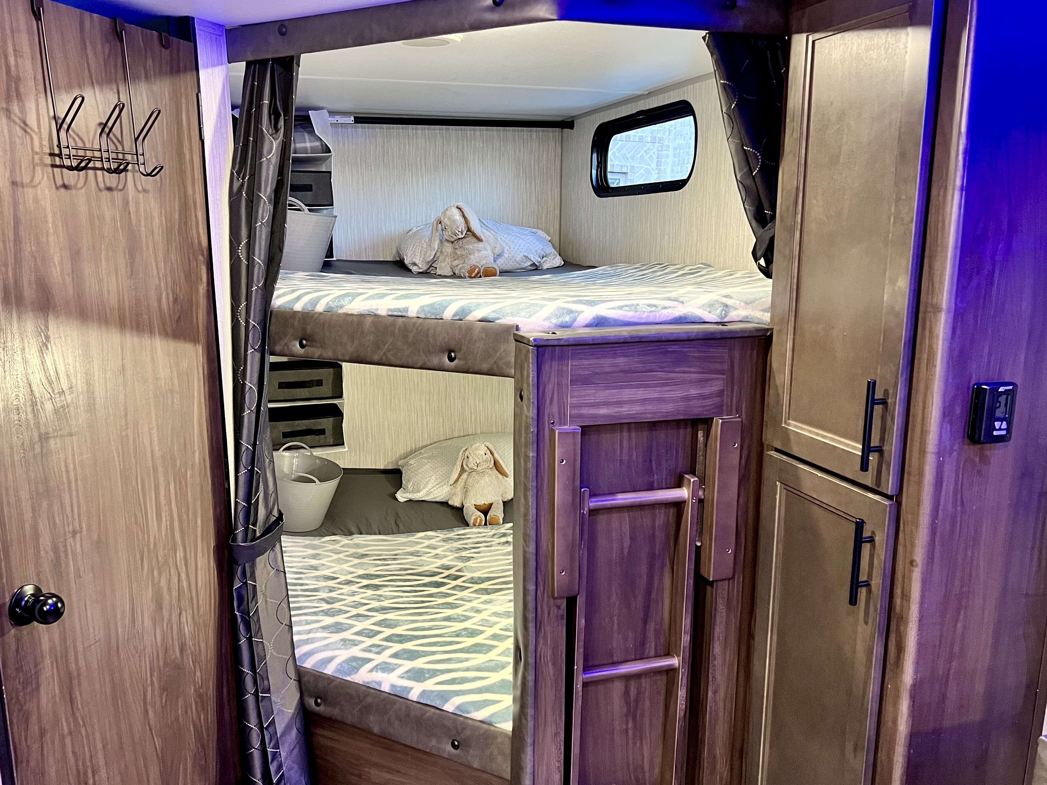 Cozy RV rental bunk beds in a neatly organized interior, complete with bedding, plush toys, storage, and window views.. Forest River Cherokee Grey Wolf 2021