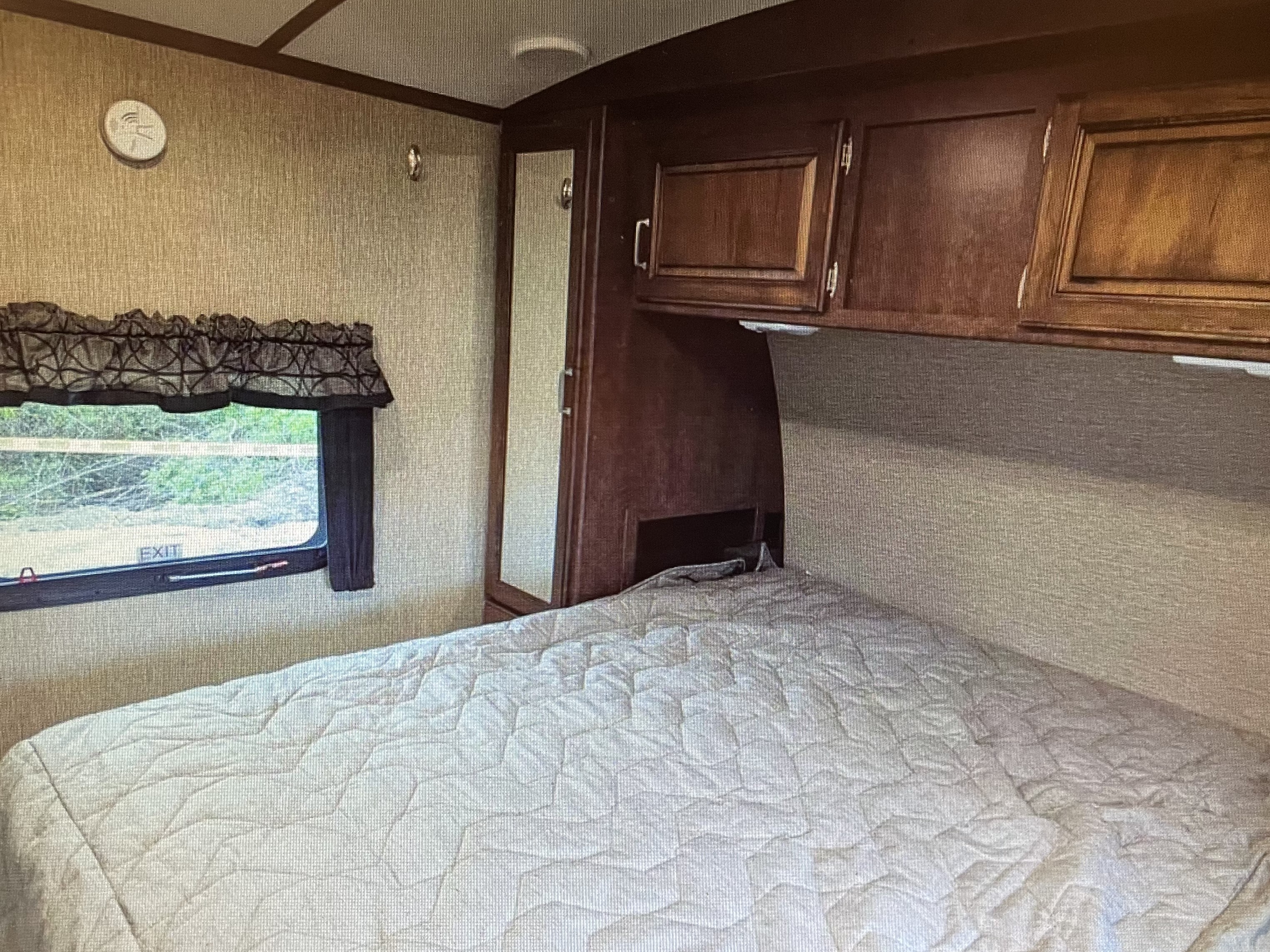 Inside an RV rental bedroom showing a bed, window with 'EXIT', wood cabinets, and a tall mirror. A comfortable mobile living space.. Keystone RV Outback Ultra-Lite 2017