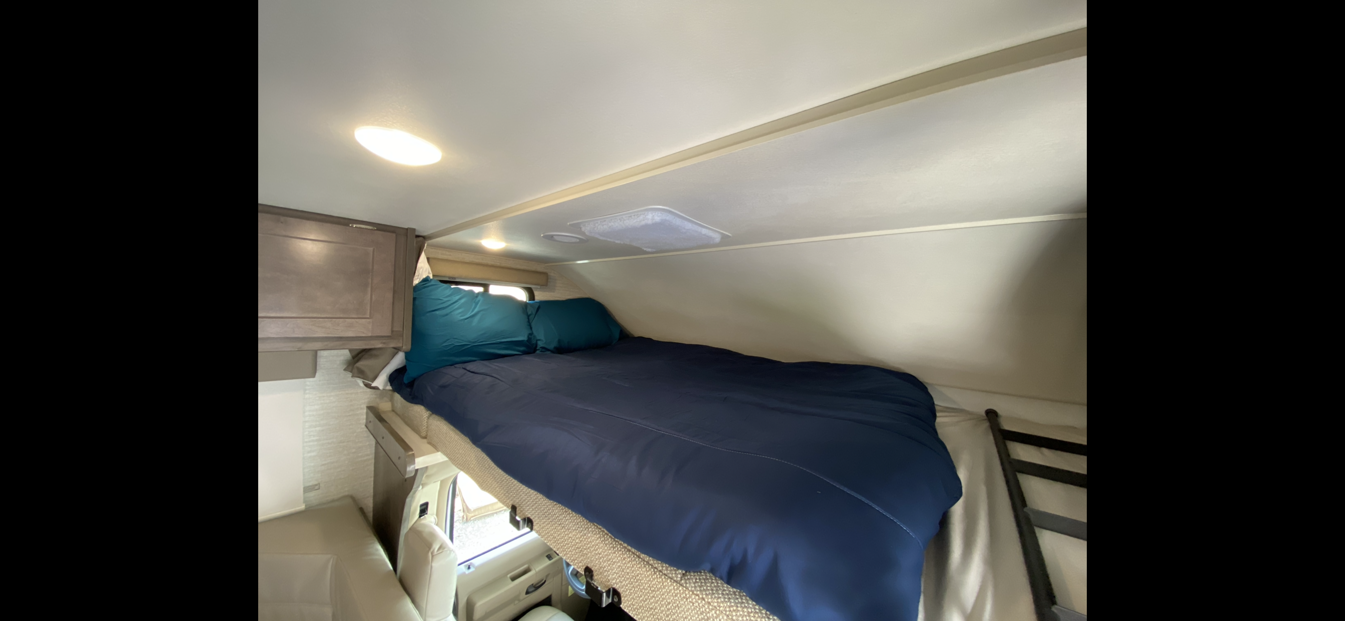 Inside an RV rental: a comfortable overhead sleeping area (bunk) with blue bedding, pillows, cabinets, and a ladder.. Winnebago Other 2023