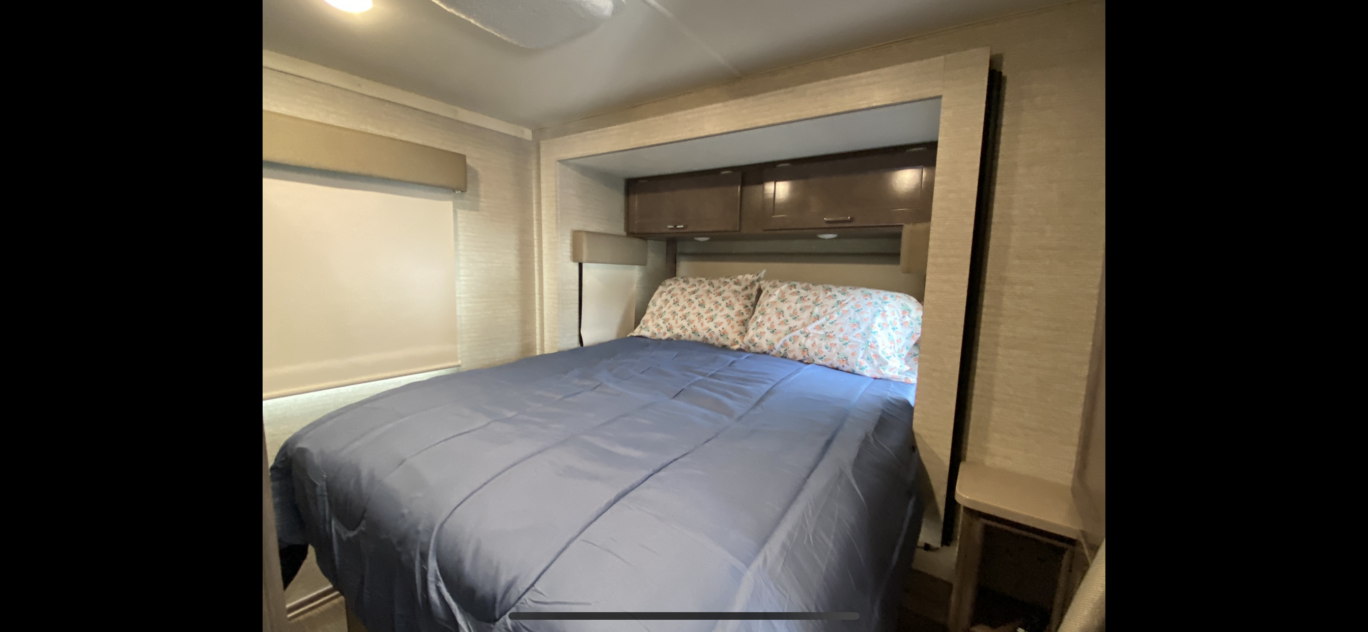 Cozy RV rental bedroom featuring a blue bed, patterned pillows, overhead cabinets, and a window for comfortable travel.. Winnebago Other 2023