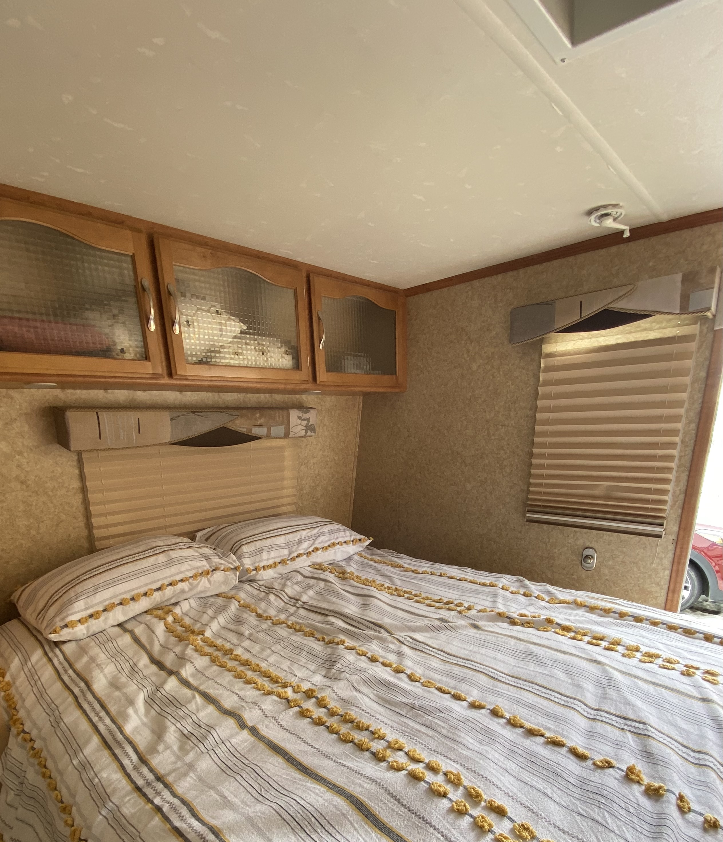 Explore this RV rental bedroom: cozy bed with unique yellow-accented bedding, storage cabinets, and window blinds.. Komfort Komfort Trailer 2008