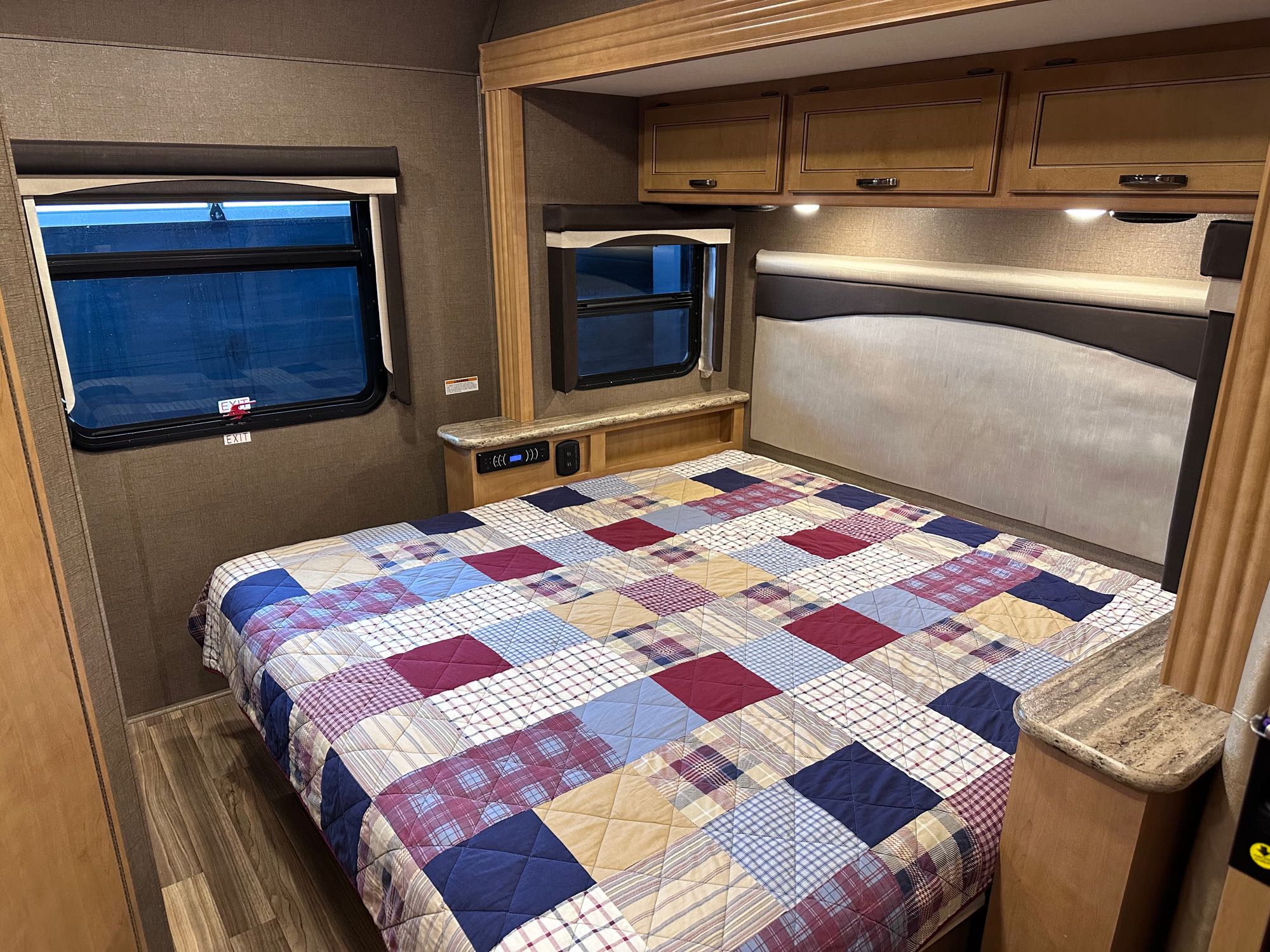 Cozy RV rental bedroom with a large bed, colorful quilt, and natural light from side windows. Perfect for your next adventure!. Thor A.C.E. 2017