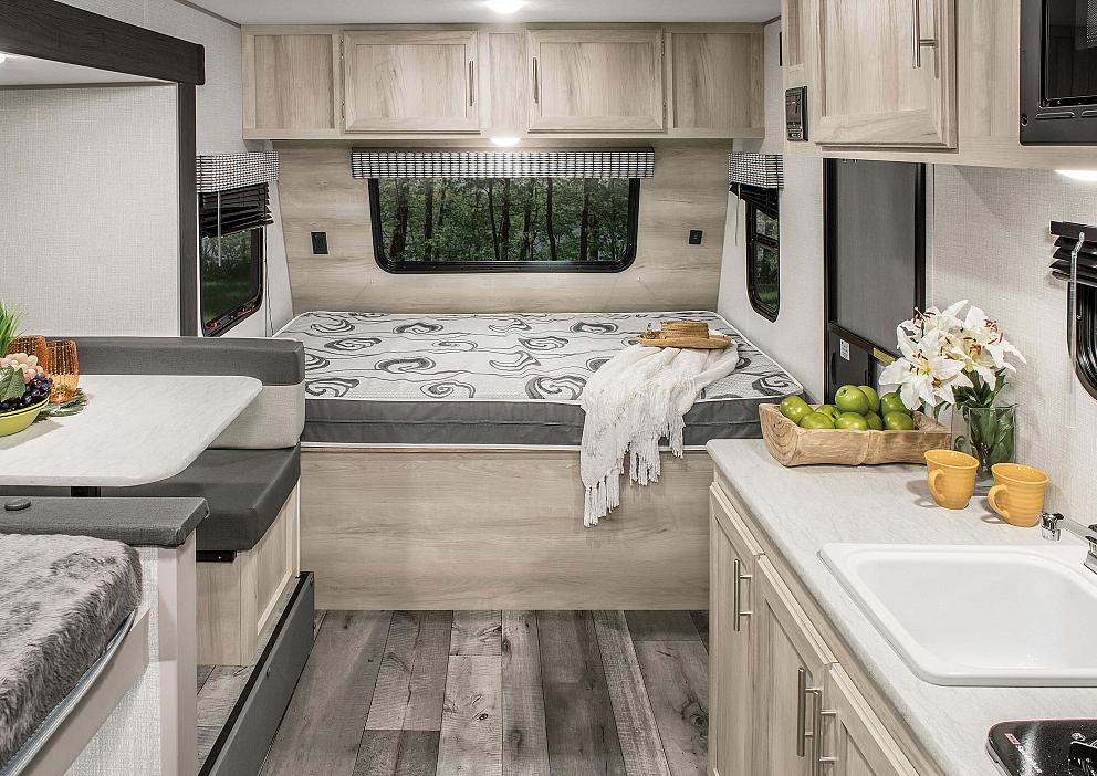 Inside a modern RV rental: a compact living space with bed, dinette, and kitchen area, designed for comfortable travel.. KZ Sportsmen 2021
