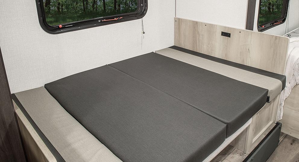 Inside an RV rental: a versatile dinette converts to a bed, with gray cushions & window.. KZ Sportsmen 2021