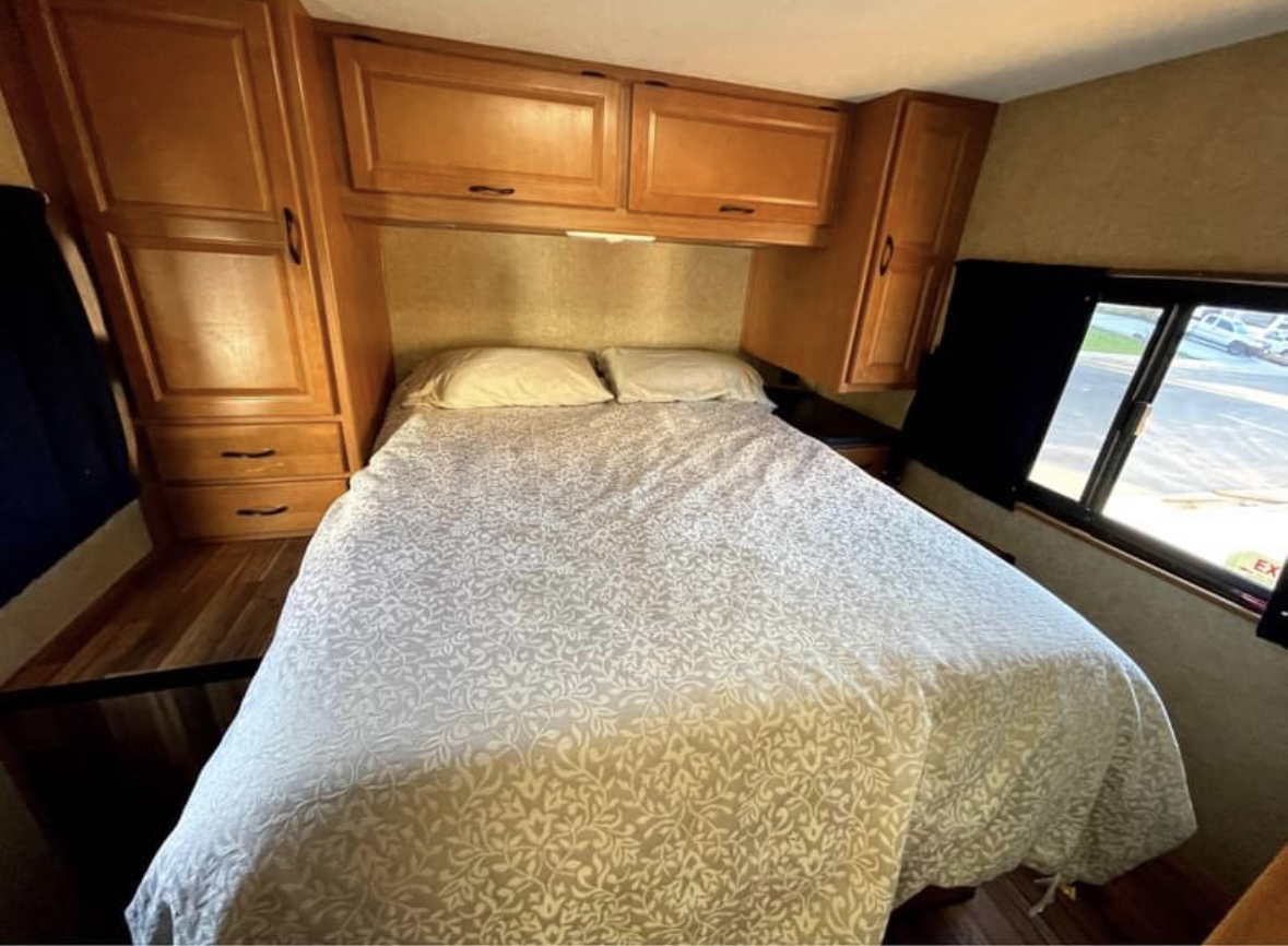 Cozy RV rental bedroom with comfortable bed, ample storage cabinets, and a window view. Perfect for travel accommodation.. Thor Majestic 2016