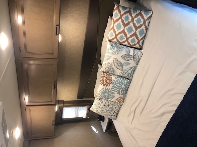 Cozy RV rental bedroom with a neatly made bed, decorative pillows, and built-in wooden cabinets.. Thor A.C.E. 2020