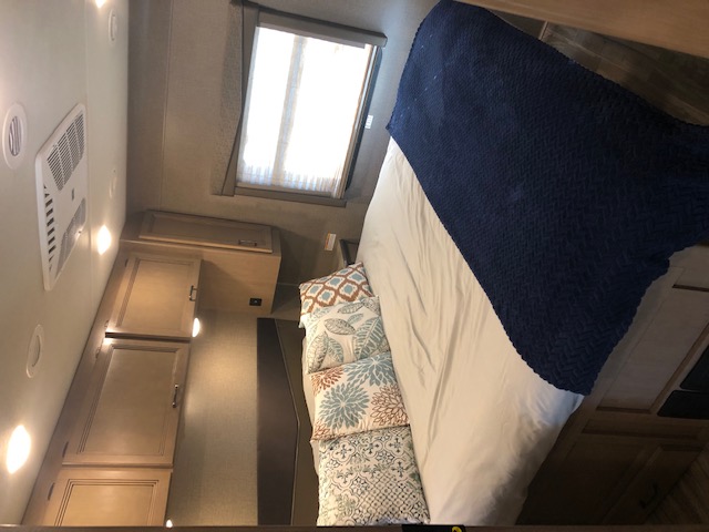 Cozy RV rental bedroom featuring a comfortable bed with a blue blanket, wood cabinets, ceiling AC, and window.. Thor A.C.E. 2020