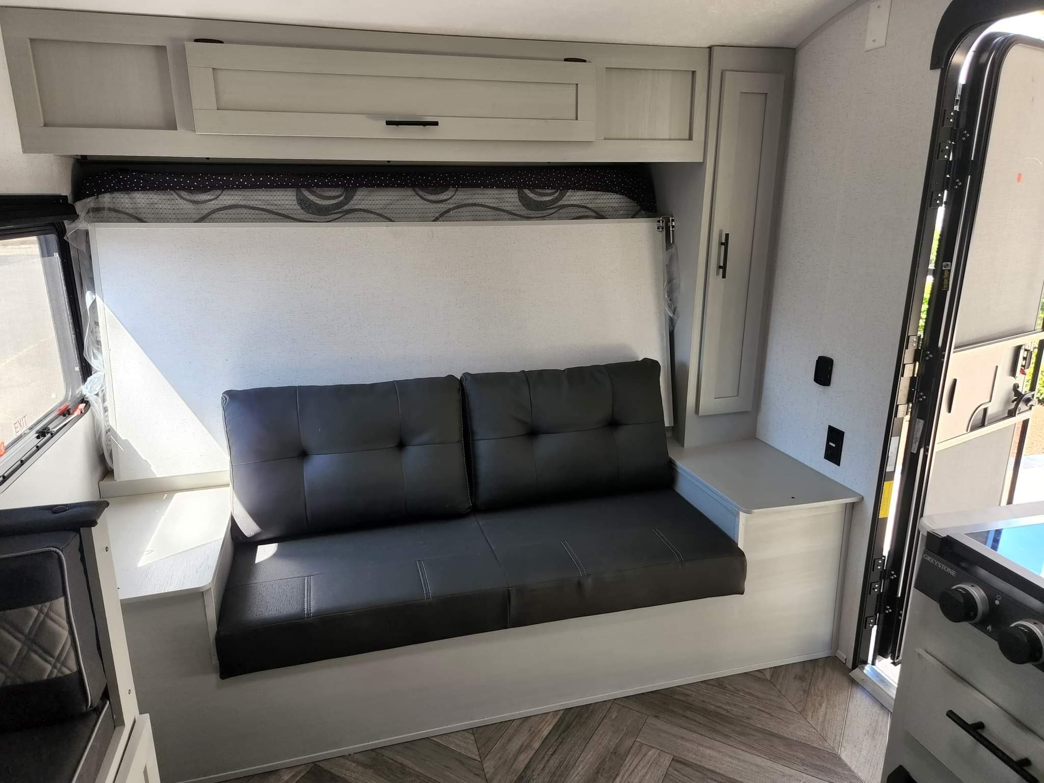 RV rental interior: main living area features a black sofa, a bed neatly folded above, light cabinets, and wood flooring.. Forest River Wildwood FSX 2022