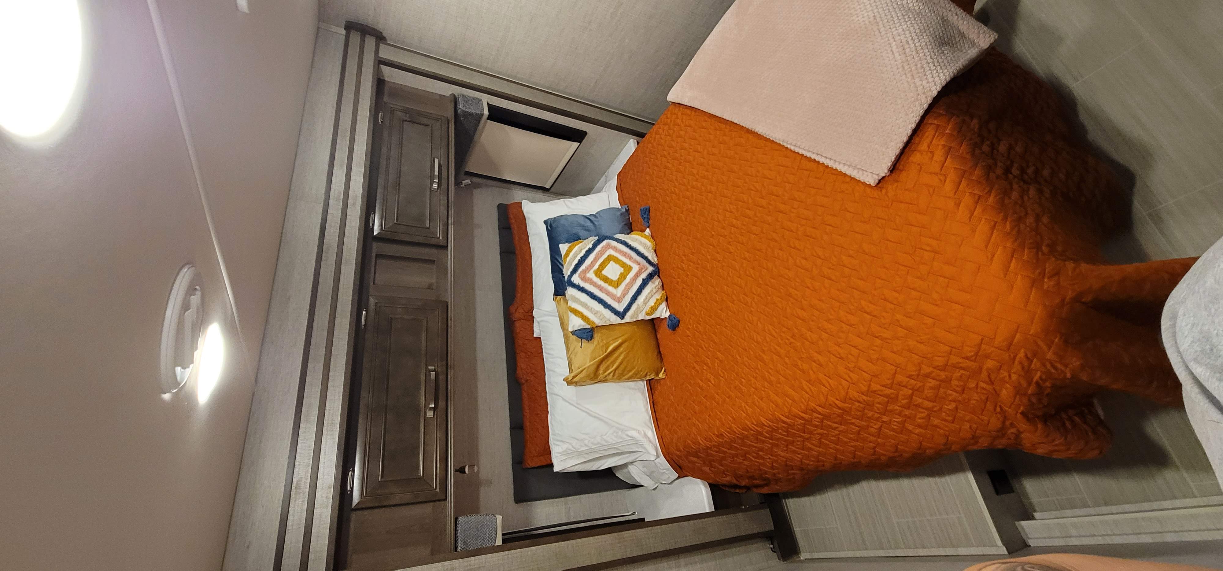 Cozy RV rental bedroom featuring a vibrant orange comforter, multiple pillows, and built-in storage.. Entegra Esteem 29v 2022