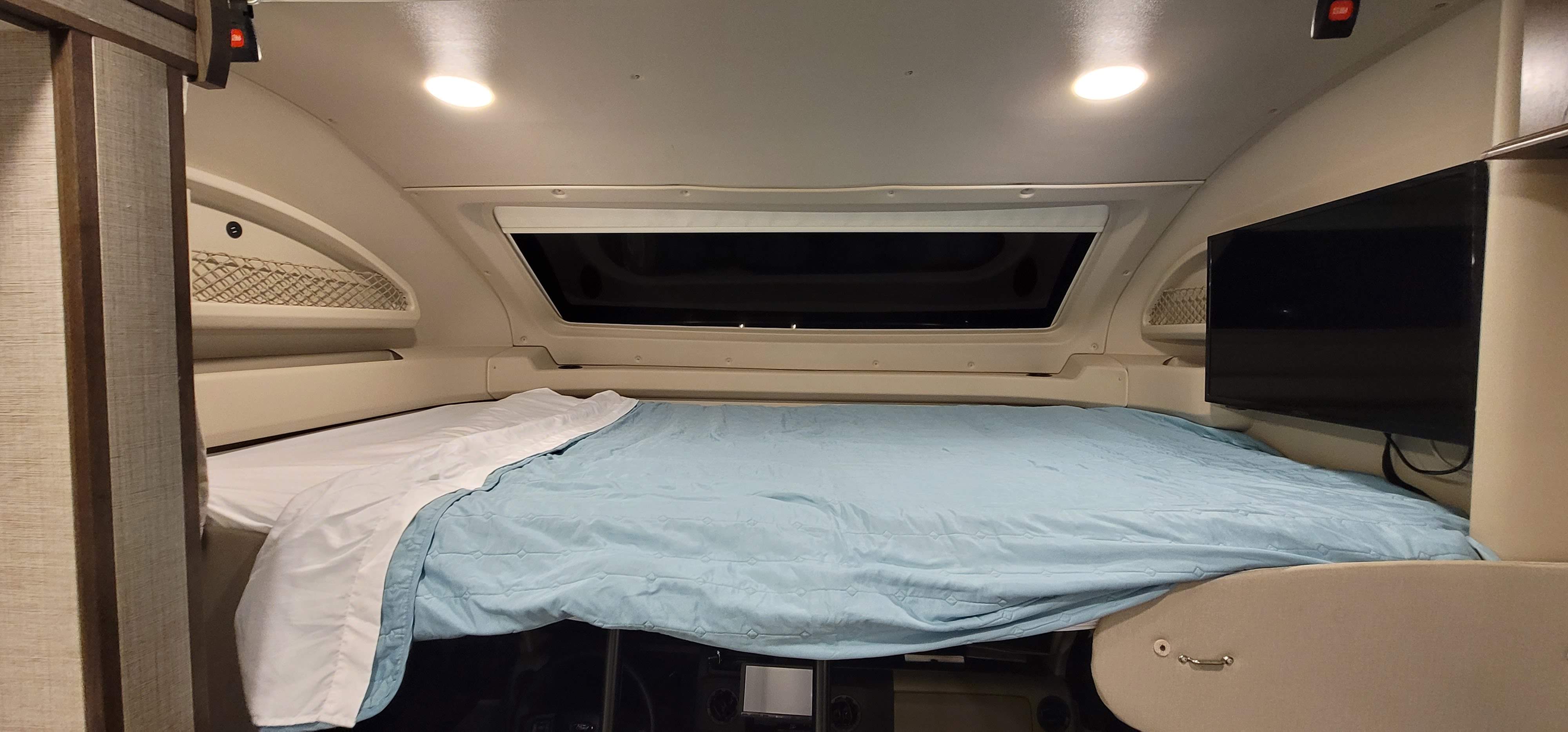 Comfortable RV rental sleeping area featuring a bed, overhead window, TV, and convenient storage netting.. Entegra Esteem 29v 2022