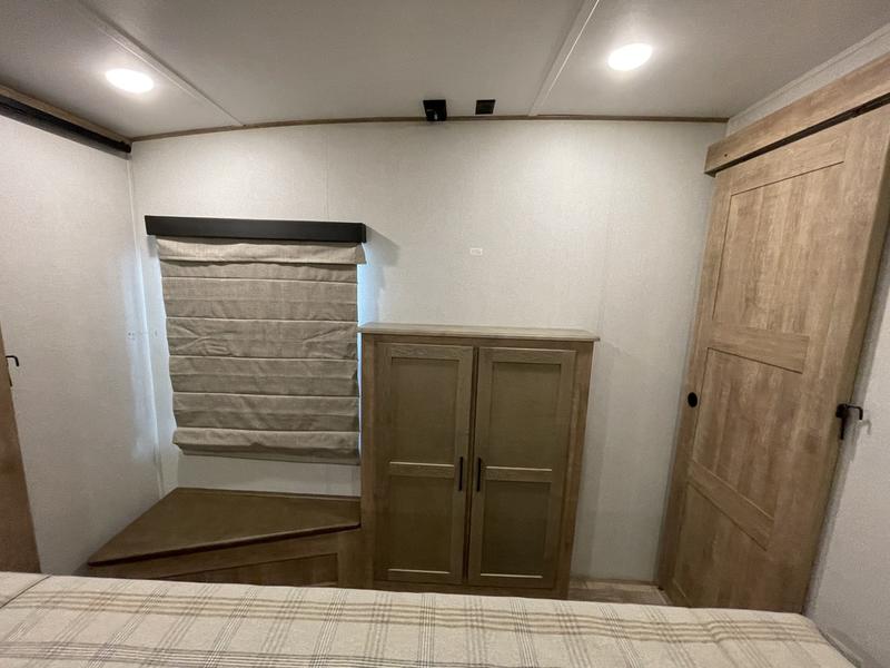 Spacious RV rental bedroom featuring light wood furniture, including a cabinet, corner bench, and sliding door, plus a window.. Keystone RV Arcadia 2022