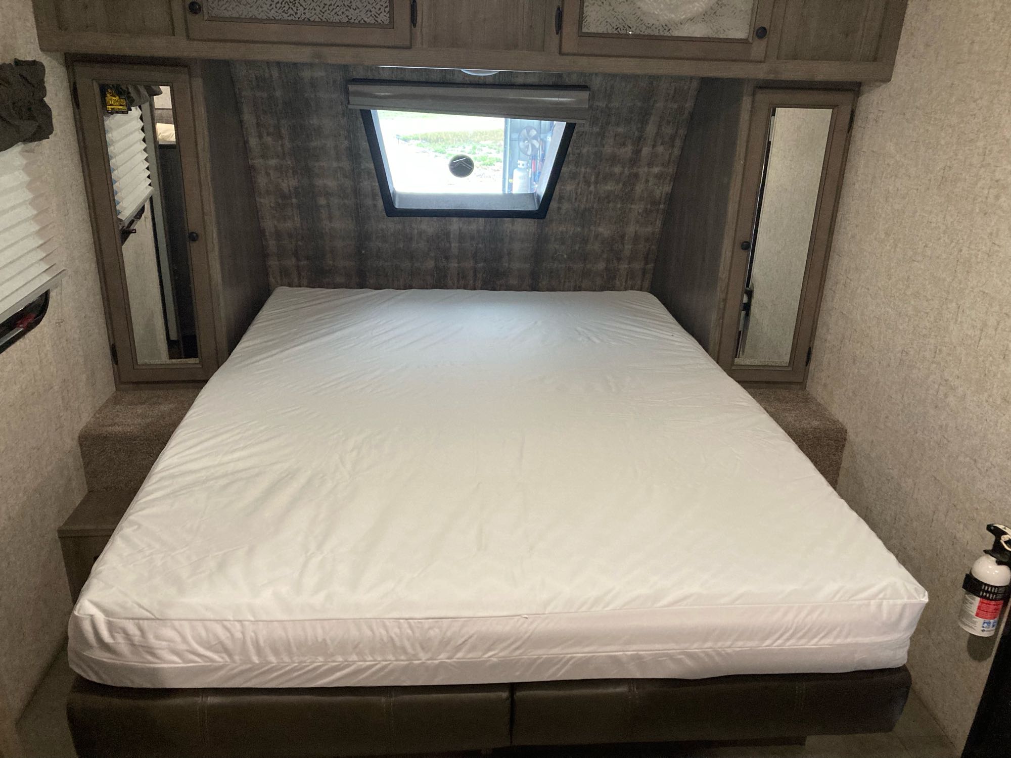 RV rental bedroom with a large white bed, overhead cabinets, window, and mirrored wardrobe doors.. Coachmen Apex Nano 2020