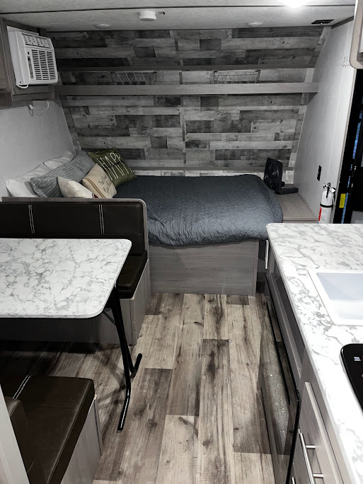 Inside a modern RV rental: bed, dinette, and kitchenette with wood-look floors. Ideal for travel and compact living.. Dutchmen Coleman Lantern LT 2023