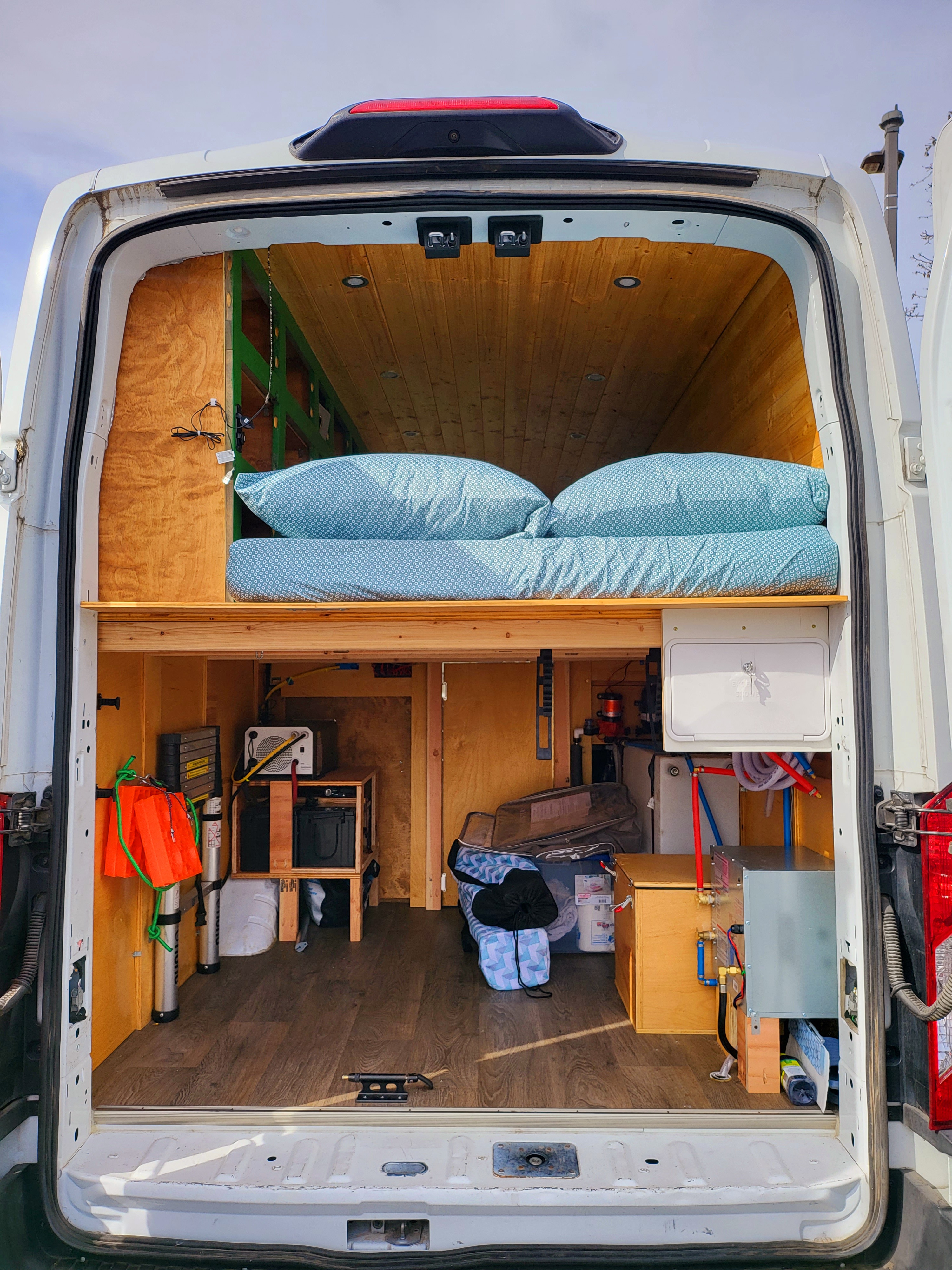 RV rental interior: A custom camper van setup with a raised bed, under-bed storage, and utility systems.. Ford Transit 2019
