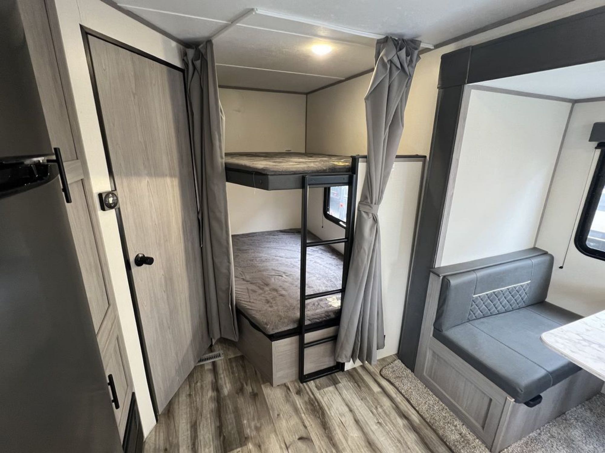 Cozy RV rental interior: bunk beds with curtains, a grey dinette booth, and wood-look flooring for comfort.. Dutchmen Coleman Lantern LT 2022