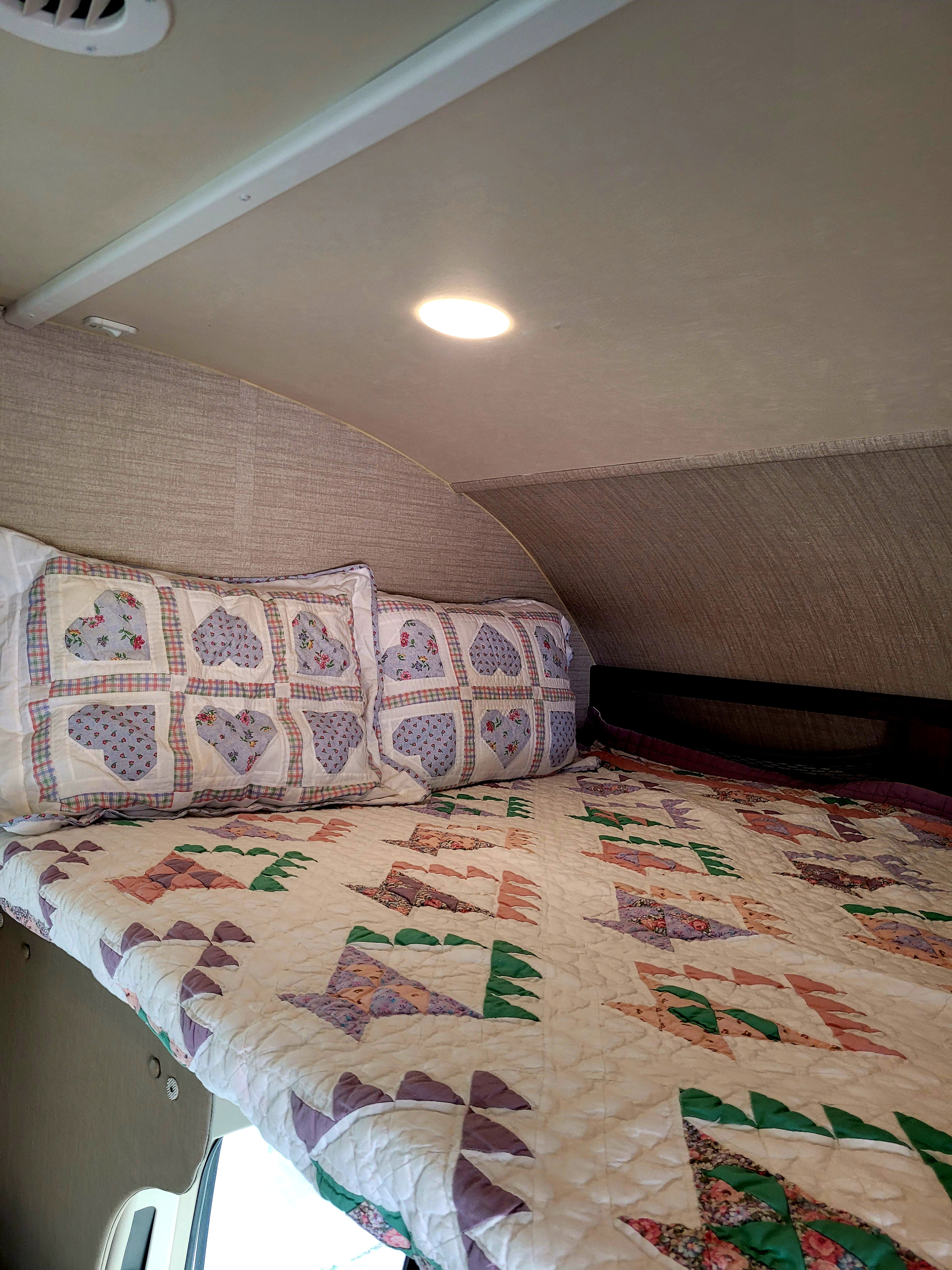 Cozy RV rental sleeping area featuring a bed with patchwork heart pillows and a colorful quilt, ideal for compact comfort.. Jayco Redhawk 2020