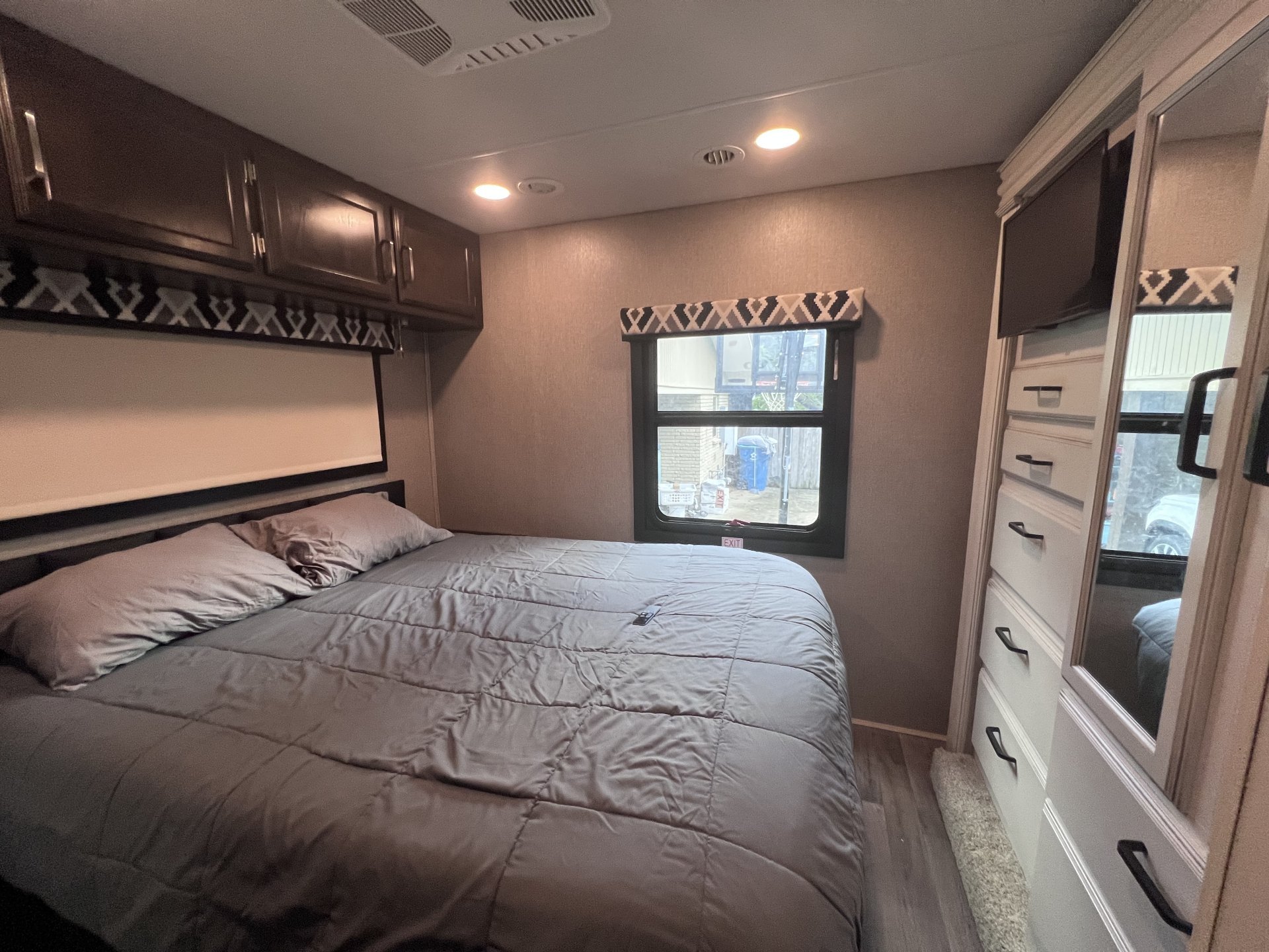 Spacious RV rental bedroom featuring a large bed, overhead cabinets, and a dresser with a TV.. Jayco Greyhawk 2021