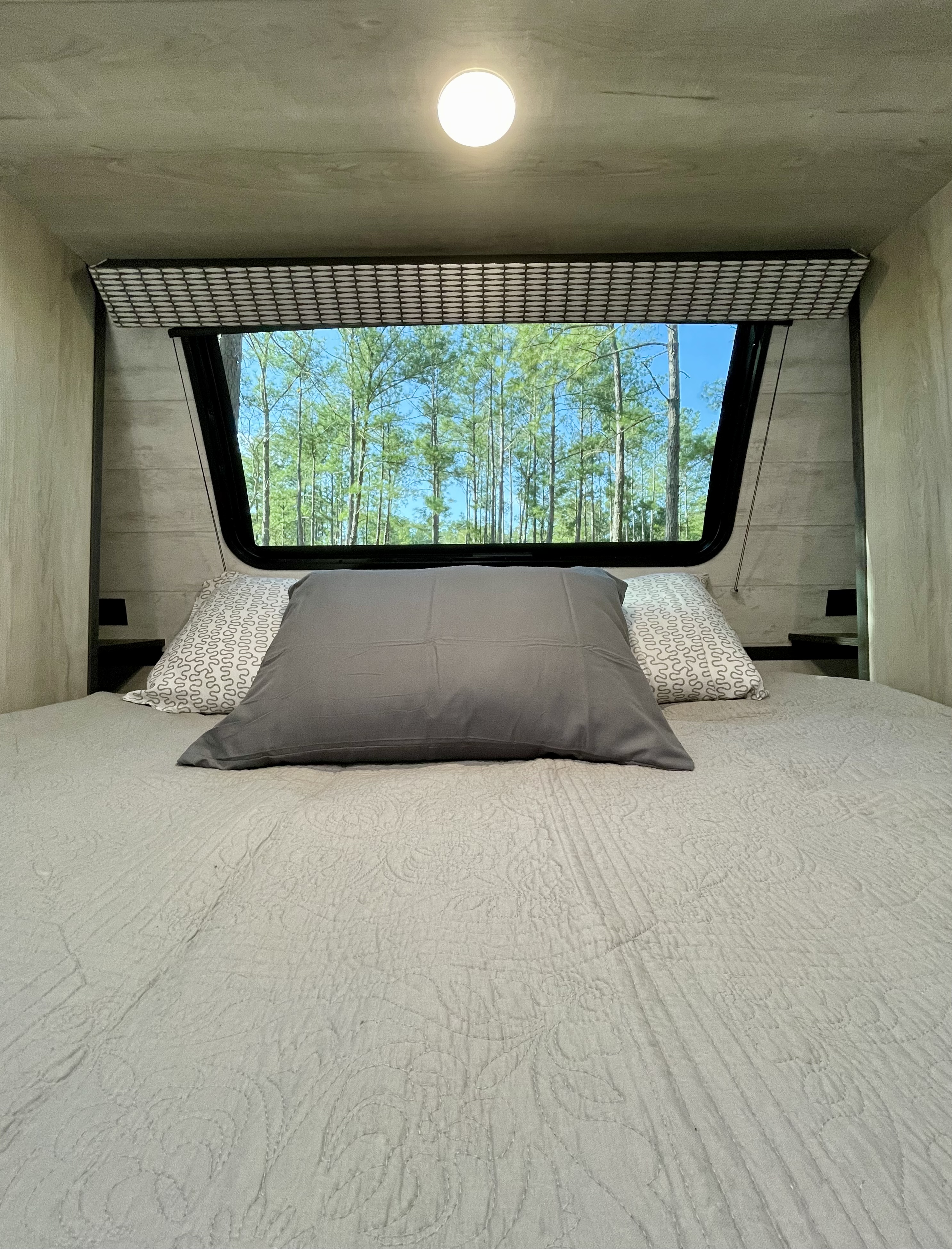 Cozy RV rental bedroom with a comfortable bed and large window offering scenic tree views.. KZ Connect 2022
