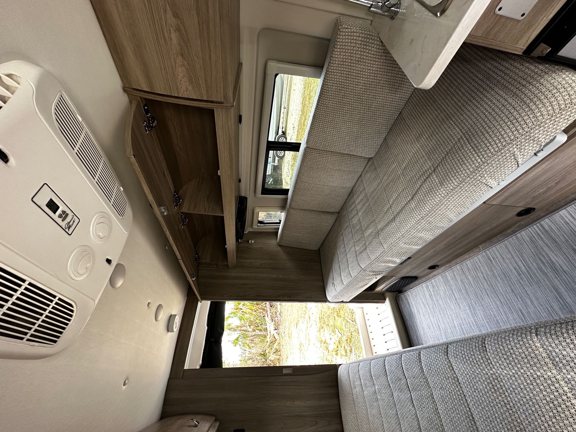 Bright RV rental interior with light wood cabinetry, a large sofa seating area, and a white AC unit on the ceiling.. Winnebago Travato 2022