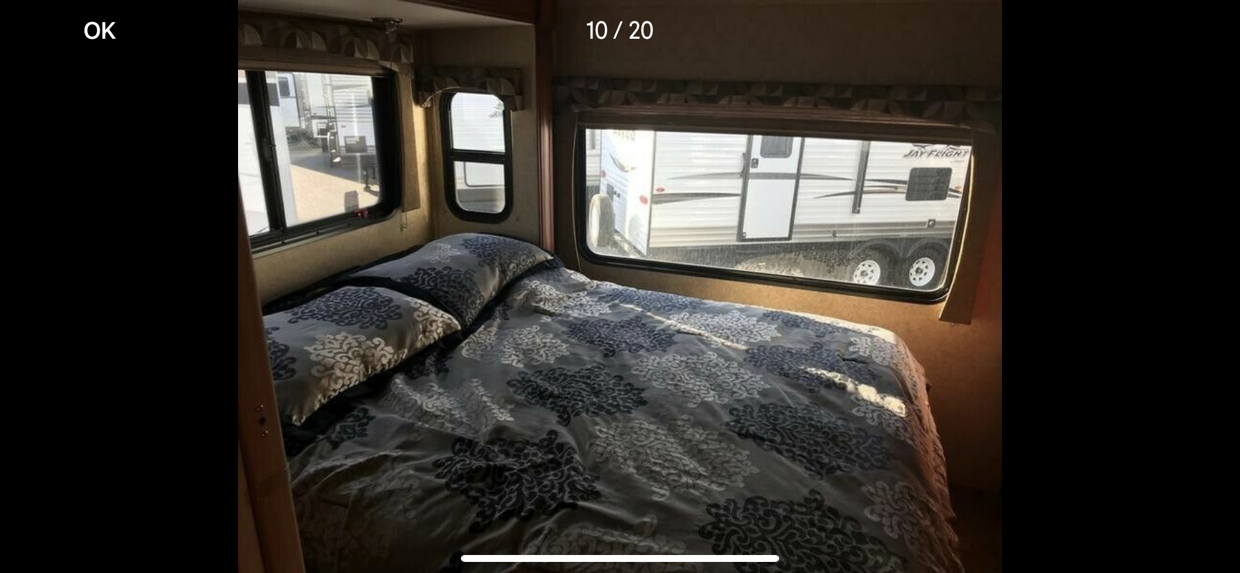 Cozy RV rental bedroom featuring a patterned bed and windows looking out to other trailers. Ideal for travel!. Forest River Sunseeker 2014