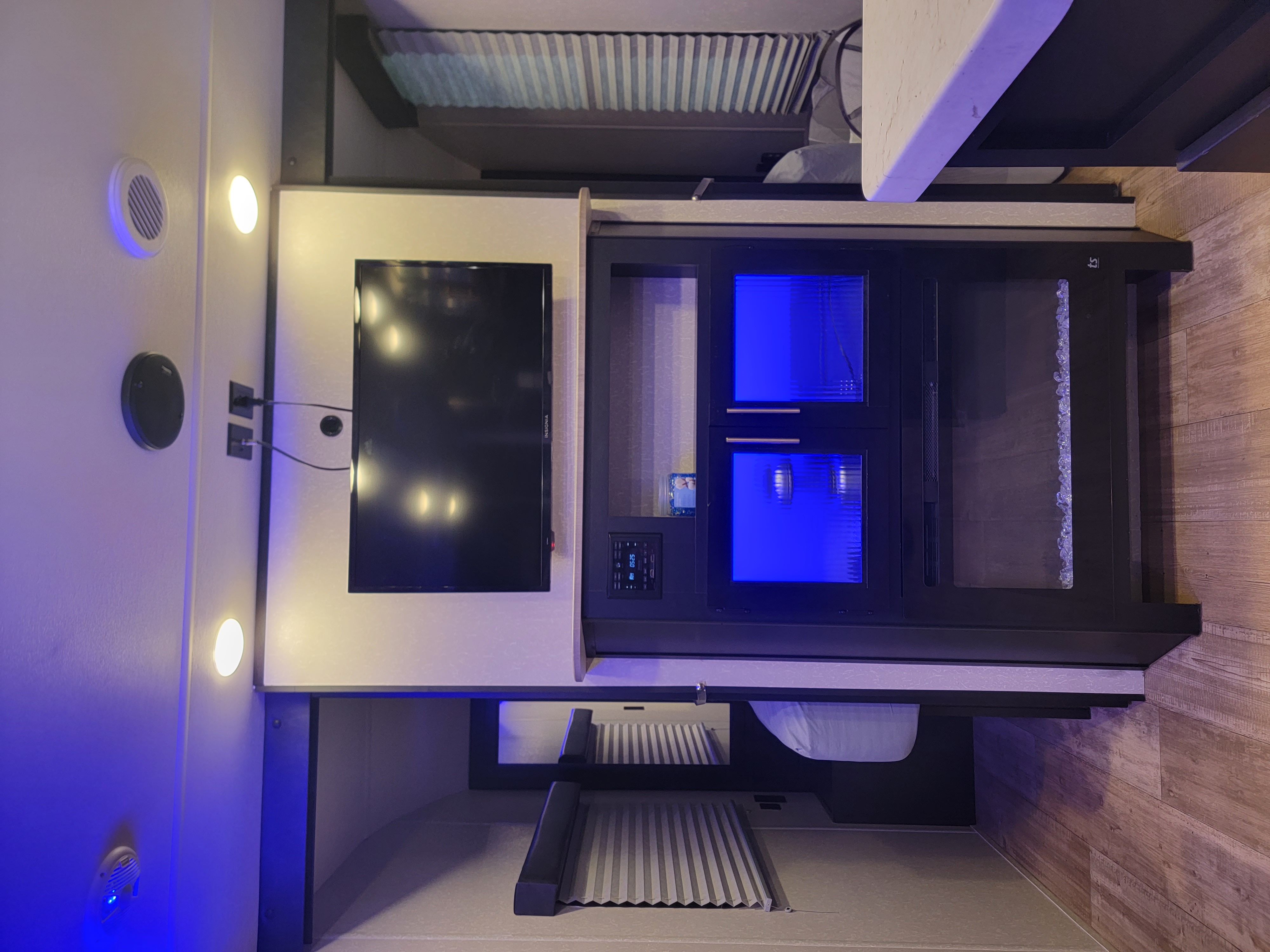 Modern RV rental interior with a wall-mounted TV, electric fireplace with blue glow, and cozy bunk beds.. Forest River Cherokee Grey Wolf 2021