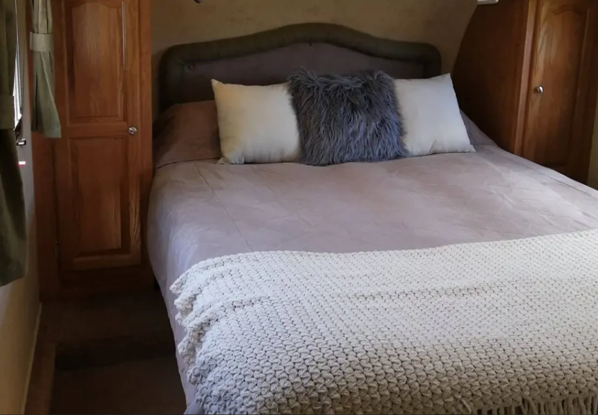 Cozy RV rental bedroom with a comfy bed, light brown duvet, grey fluffy pillow, and white knitted throw.. Forest River Flagstaff 2010