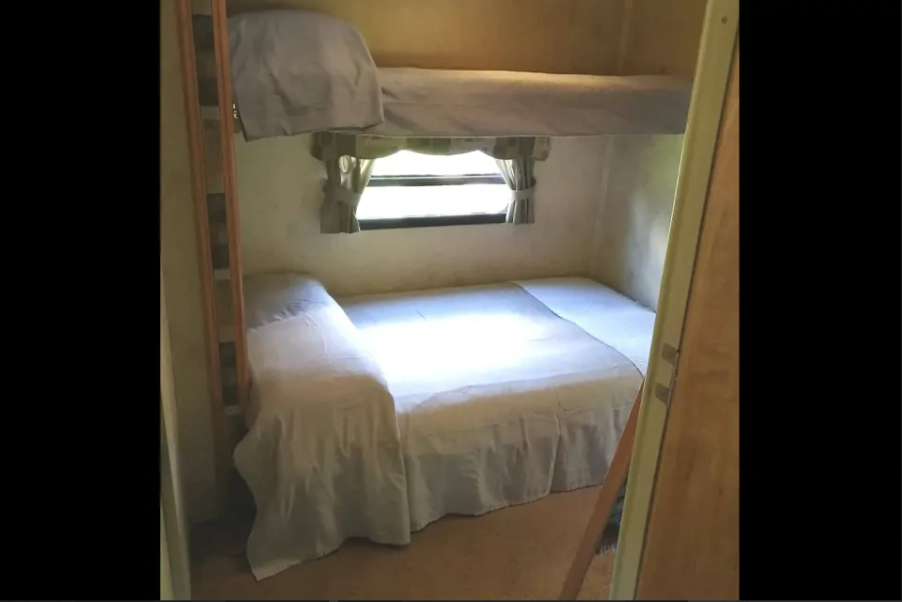 Cozy RV rental sleeping area featuring bunk beds and a lower bed with white linens, ideal for travel.. Forest River Flagstaff 2010
